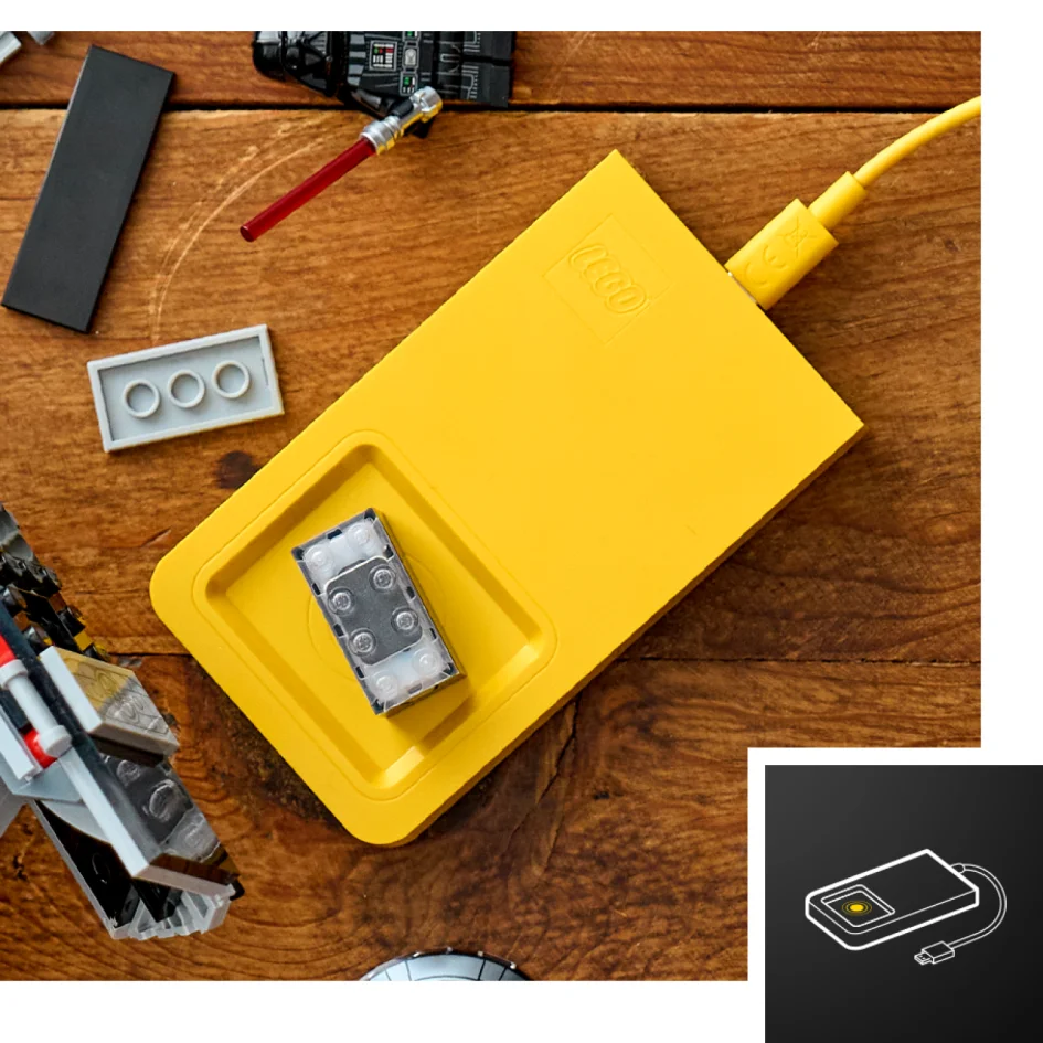 Imagine cu un încărcător portabil LEGO, galben, și piese LEGO împrăștiate pe o suprafață de lemn.