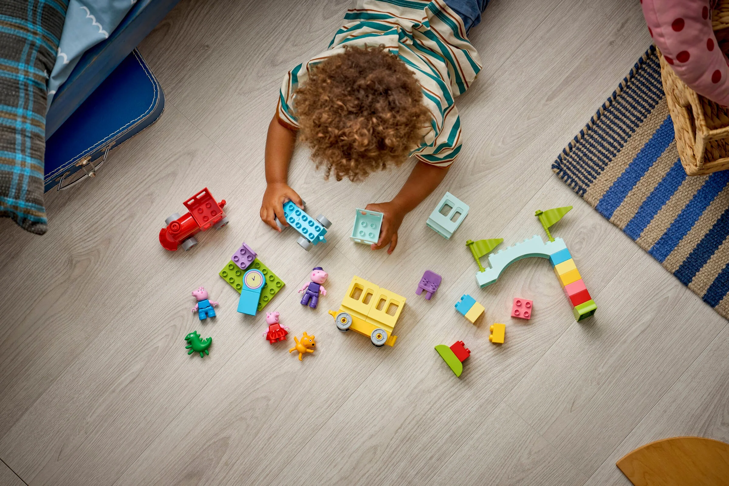 Copil jucându-se cu setul LEGO Duplo Trenulețul cu Bunicul Pig pe podea. Piesele sunt colorate.