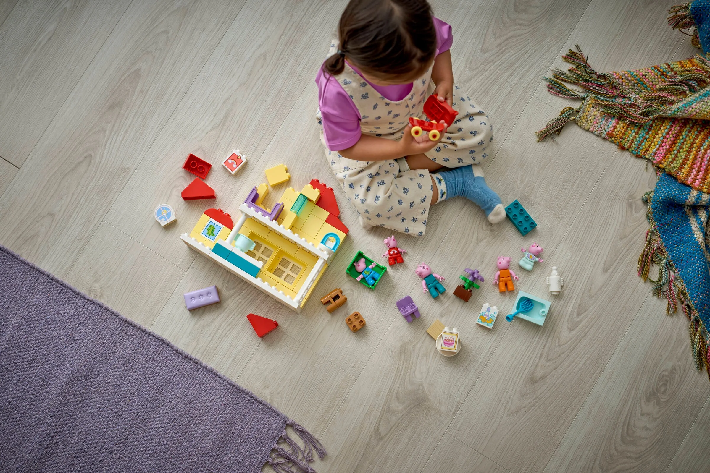 Copil se joacă cu setul LEGO DUPLO 10467 Casa Familiei pe o podea de lemn.