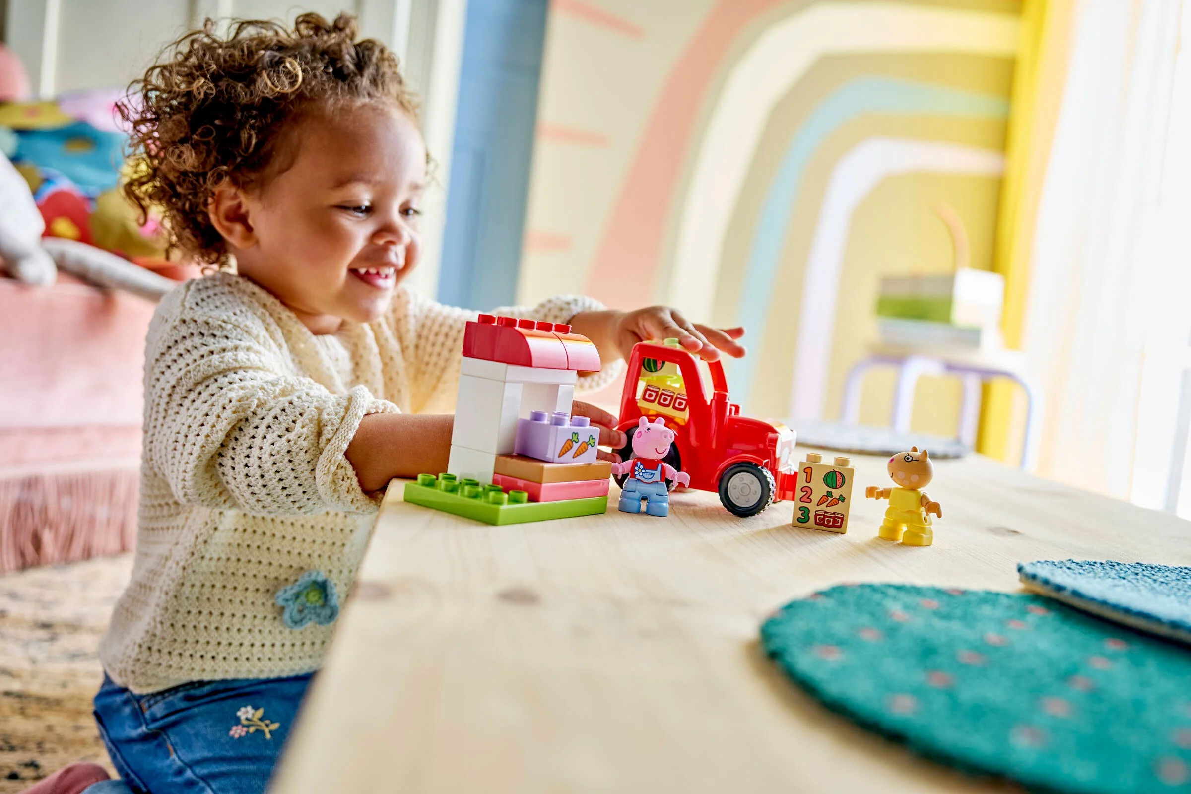 Fetiță zâmbitoare se joacă cu setul LEGO Duplo Tractor și Piață, explorând și învățând.