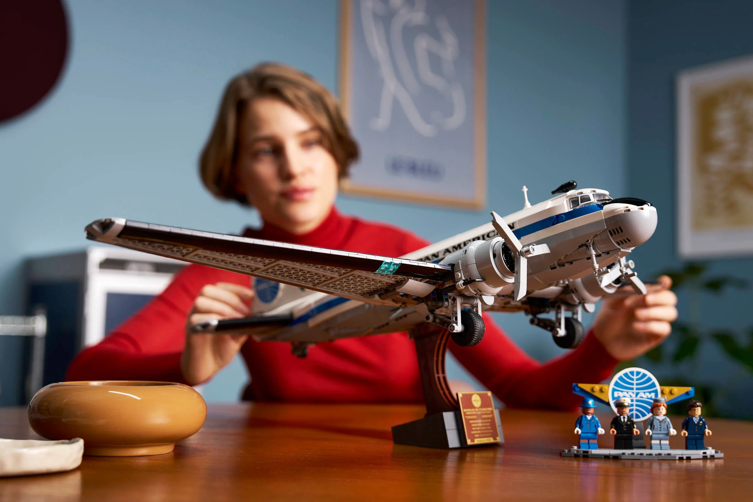 Avionul DC-3 PAN AM și minifigurinele, prezentate pe un birou de lemn, cu o persoană în fundal.