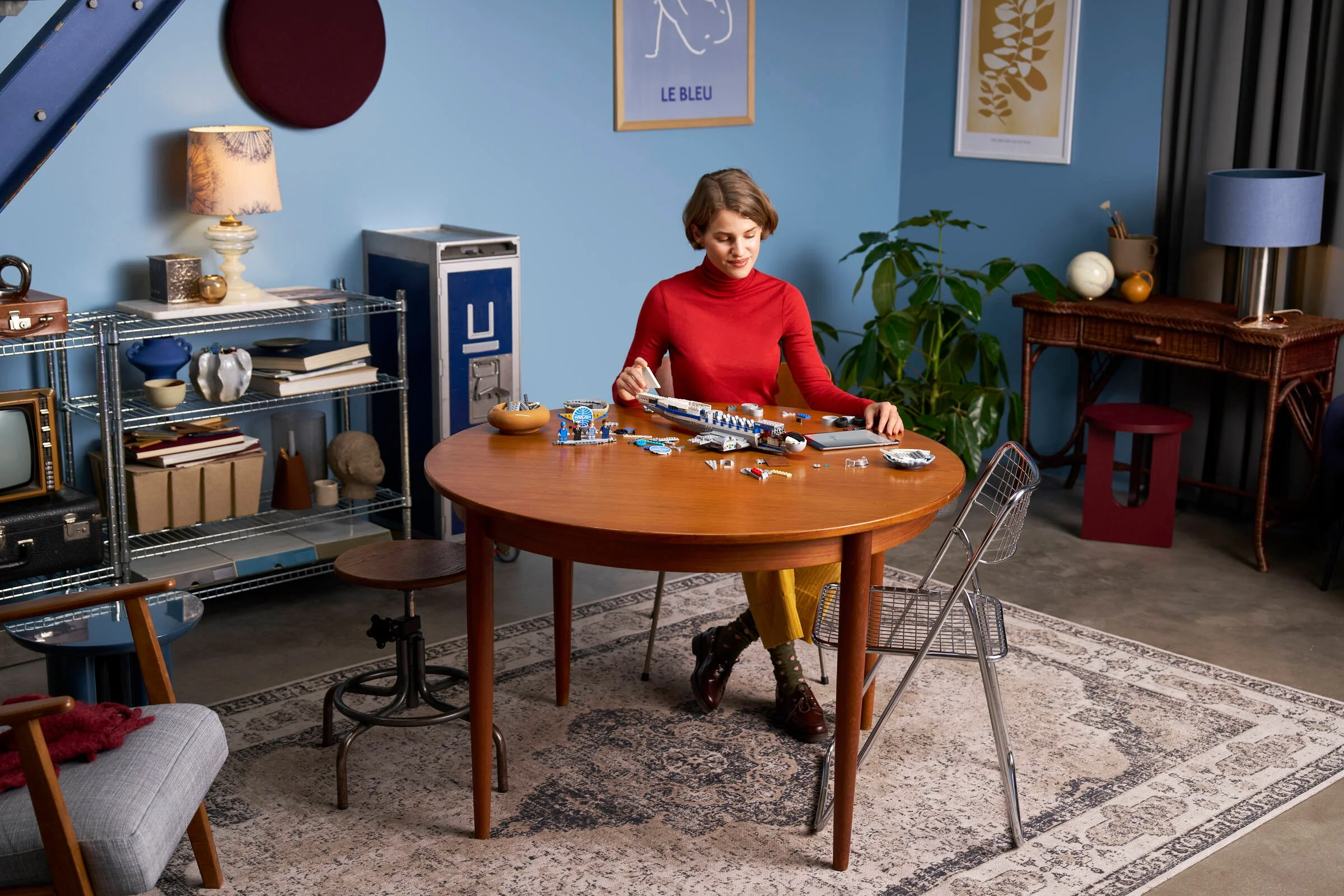 Femeie construind modelul DC-3 PAN AM de la LEGO pe o masă rotundă.