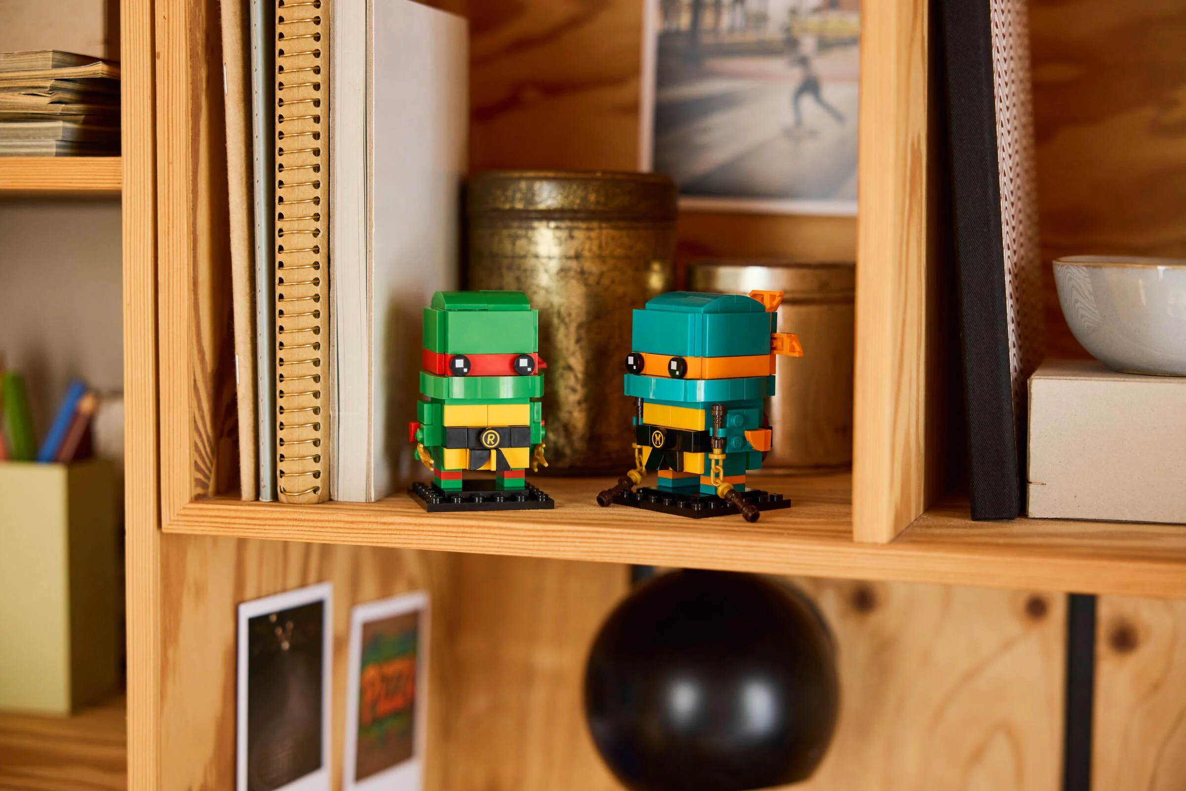 Figurinele LEGO BrickHeadz TMNT, Raphael și Michelangelo, expuse pe un raft de lemn. Detalii.