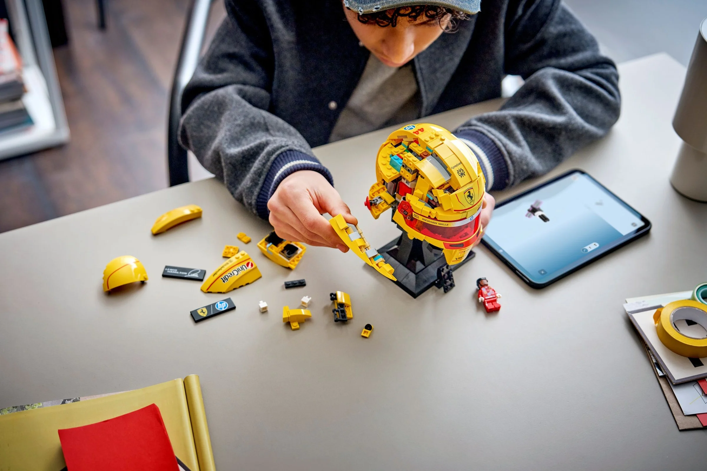 Construirea căștii LEGO Ferrari HP Lewis Hamilton. Un copil asamblează casca galbenă, cu instrucțiuni pe tabletă.