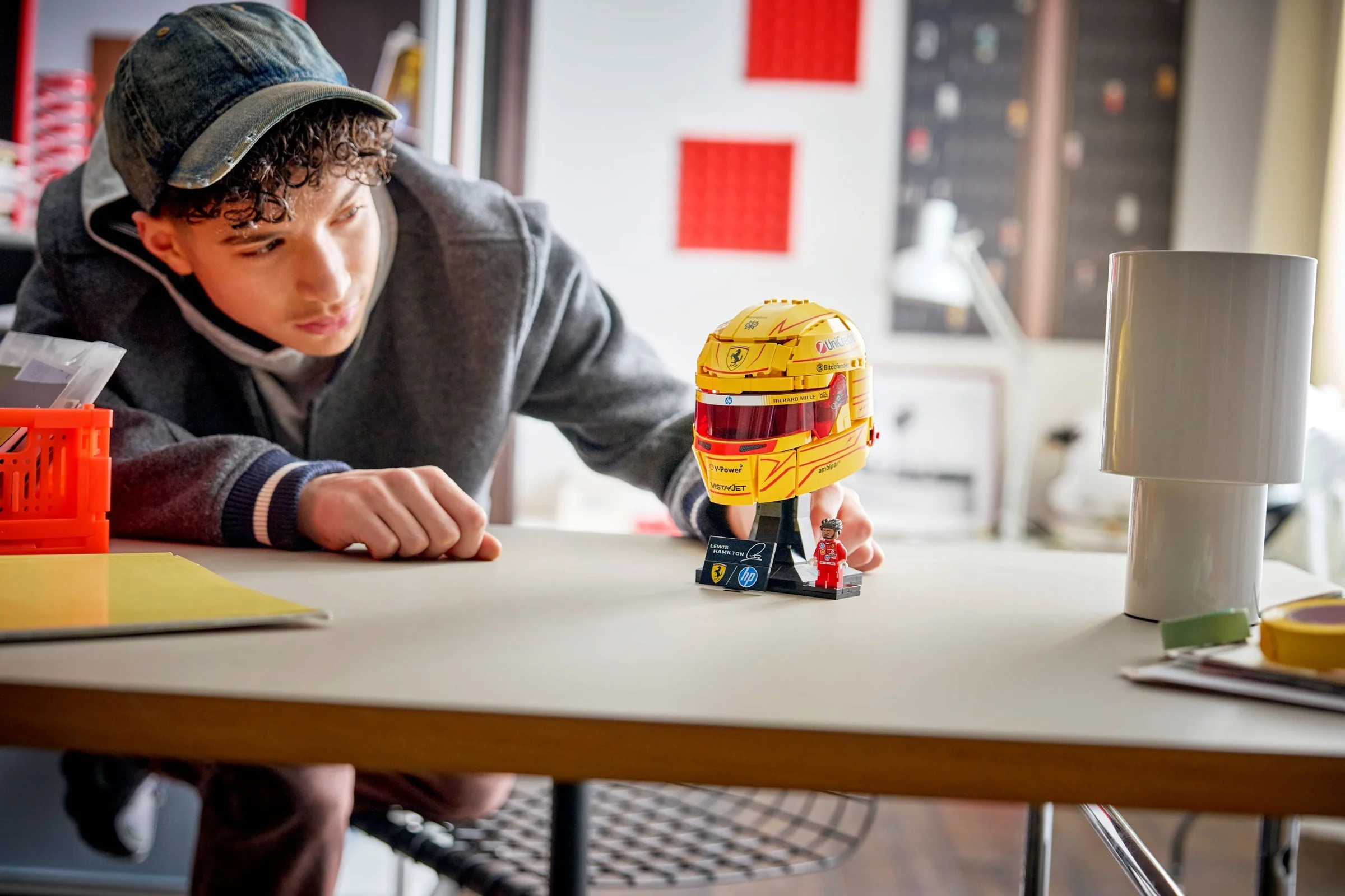 Un tânăr admiră casca LEGO Ferrari a lui Lewis Hamilton. Casca este galbenă și roșie.