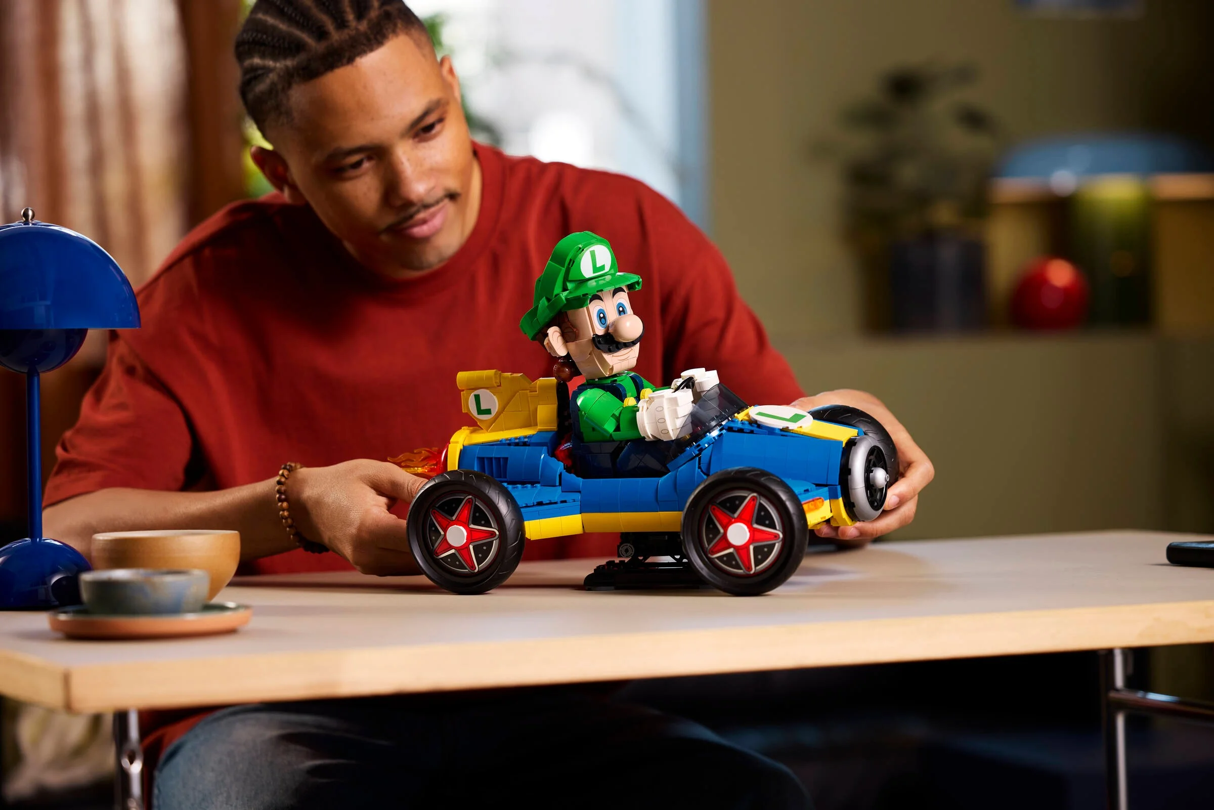 Luigi și Mach 8 LEGO pe masă, un adult admirând modelul. Perspectivă din față.