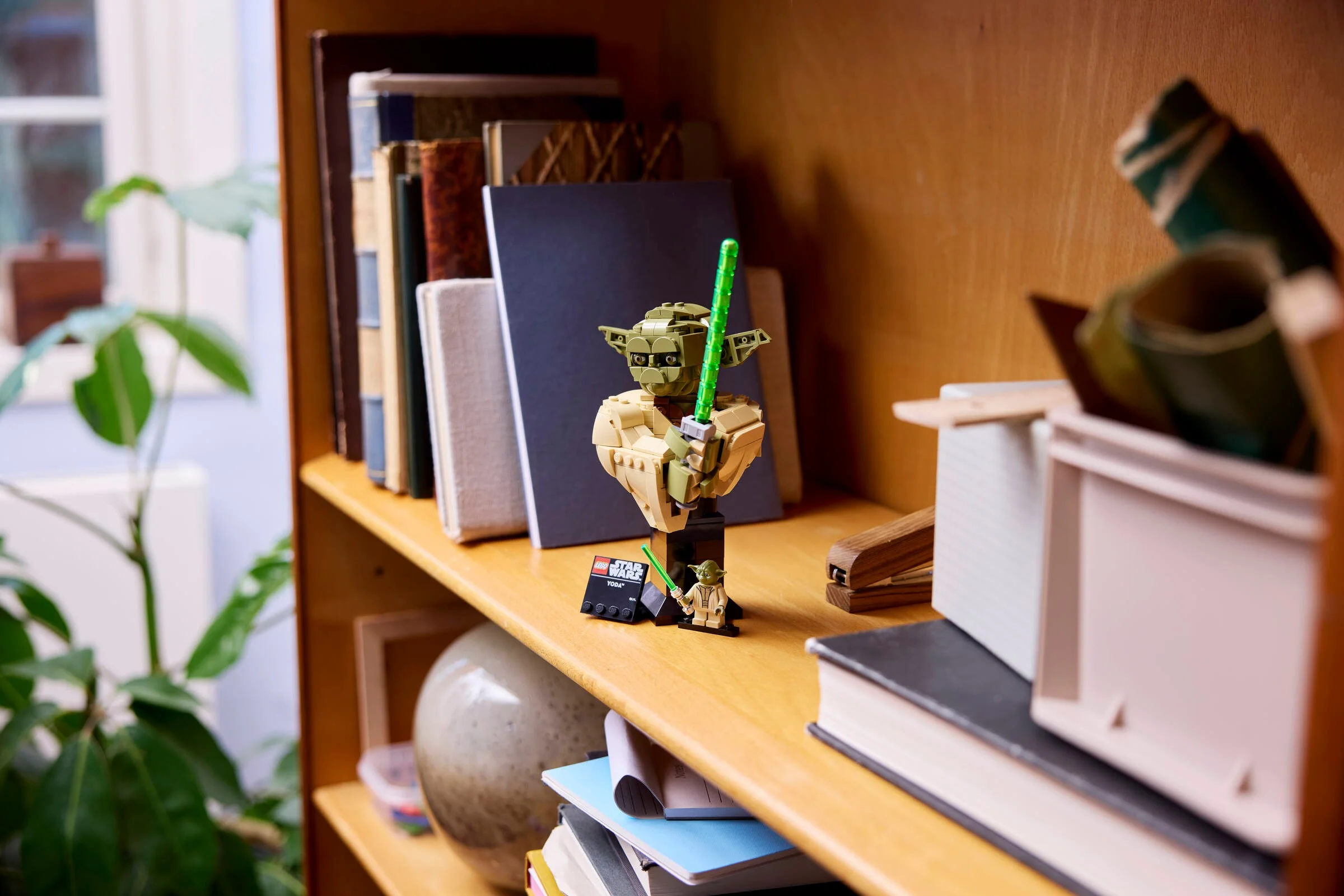 Bustul LEGO Yoda, expus pe un raft cu cărți și alte obiecte decorative. Model detaliat Star Wars.