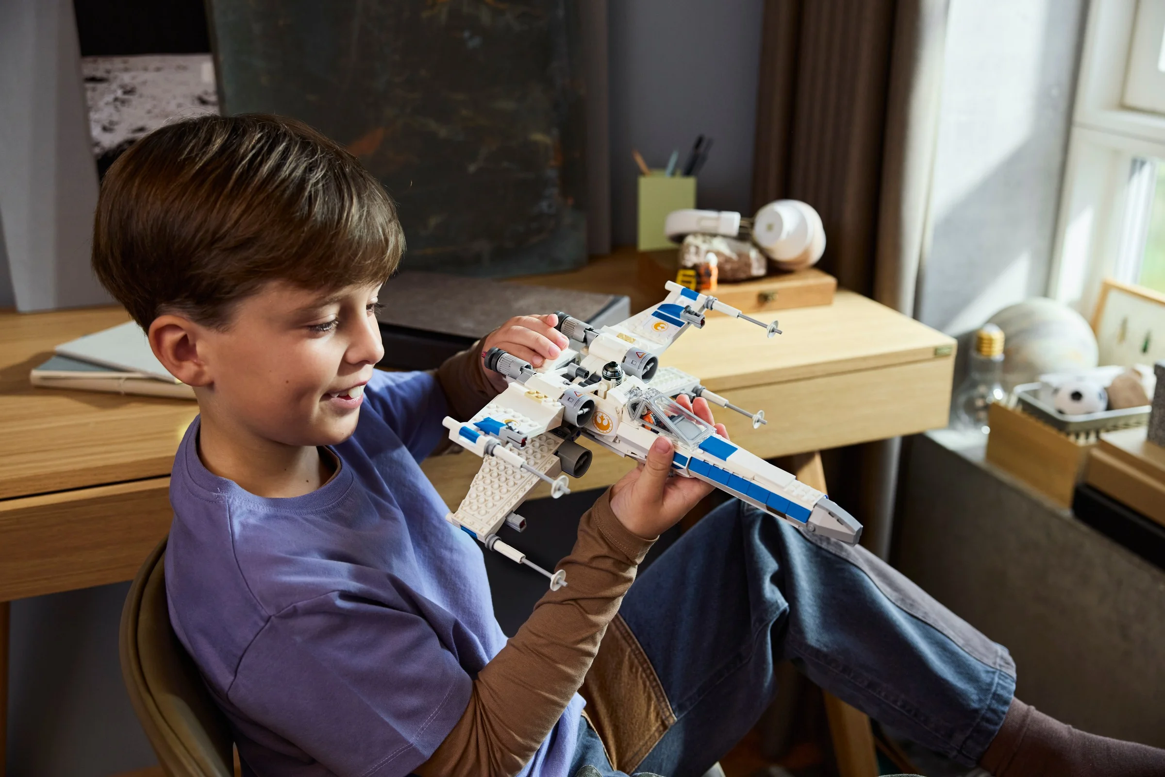 Un băiat zâmbește ținând X-wing-ul asamblat, bucuros de realizare.