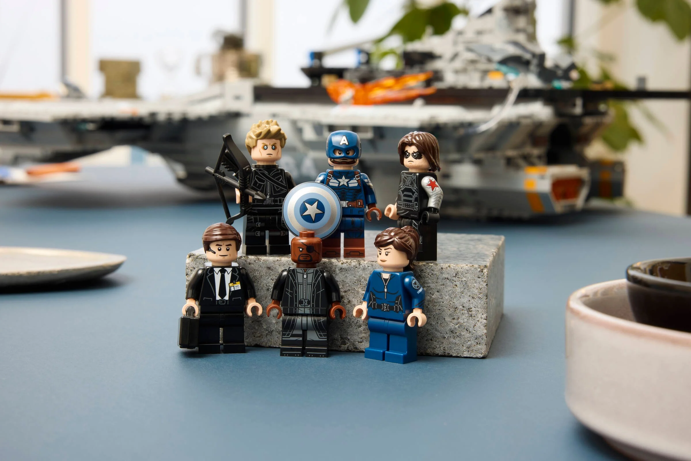Prezentare cu minifigurinele S.H.I.E.L.D., inclusiv Captain America, pe fundalul Helicarrier-ului.