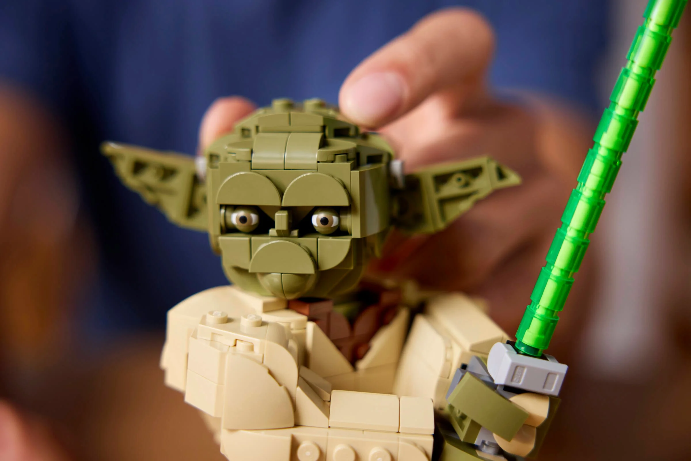 Prim-plan cu bustul LEGO Yoda, afișând detalii ale feței și sabia laser verde.
