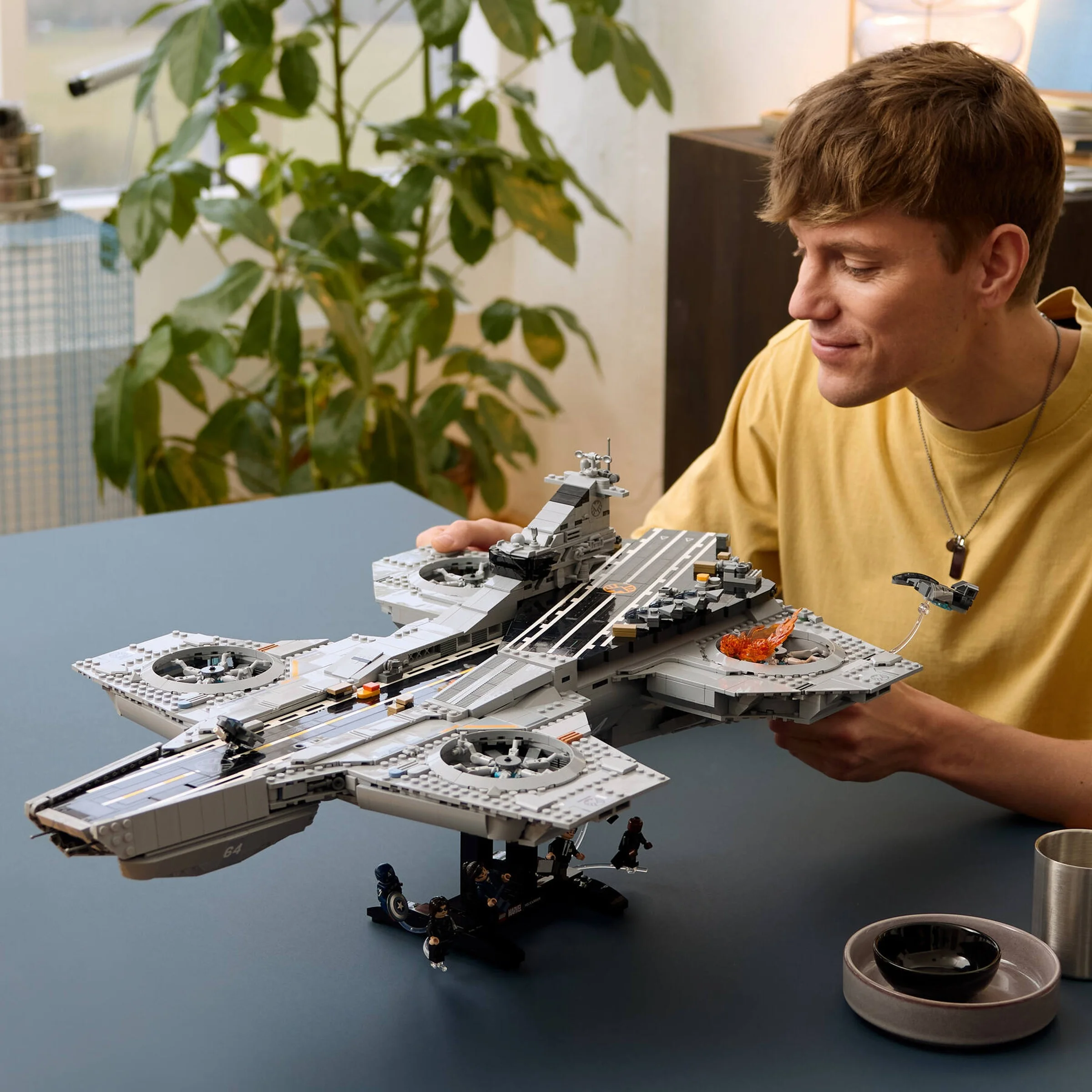 Un tânăr admiră Helicarrier-ul S.H.I.E.L.D. LEGO, arătând detaliile modelului.