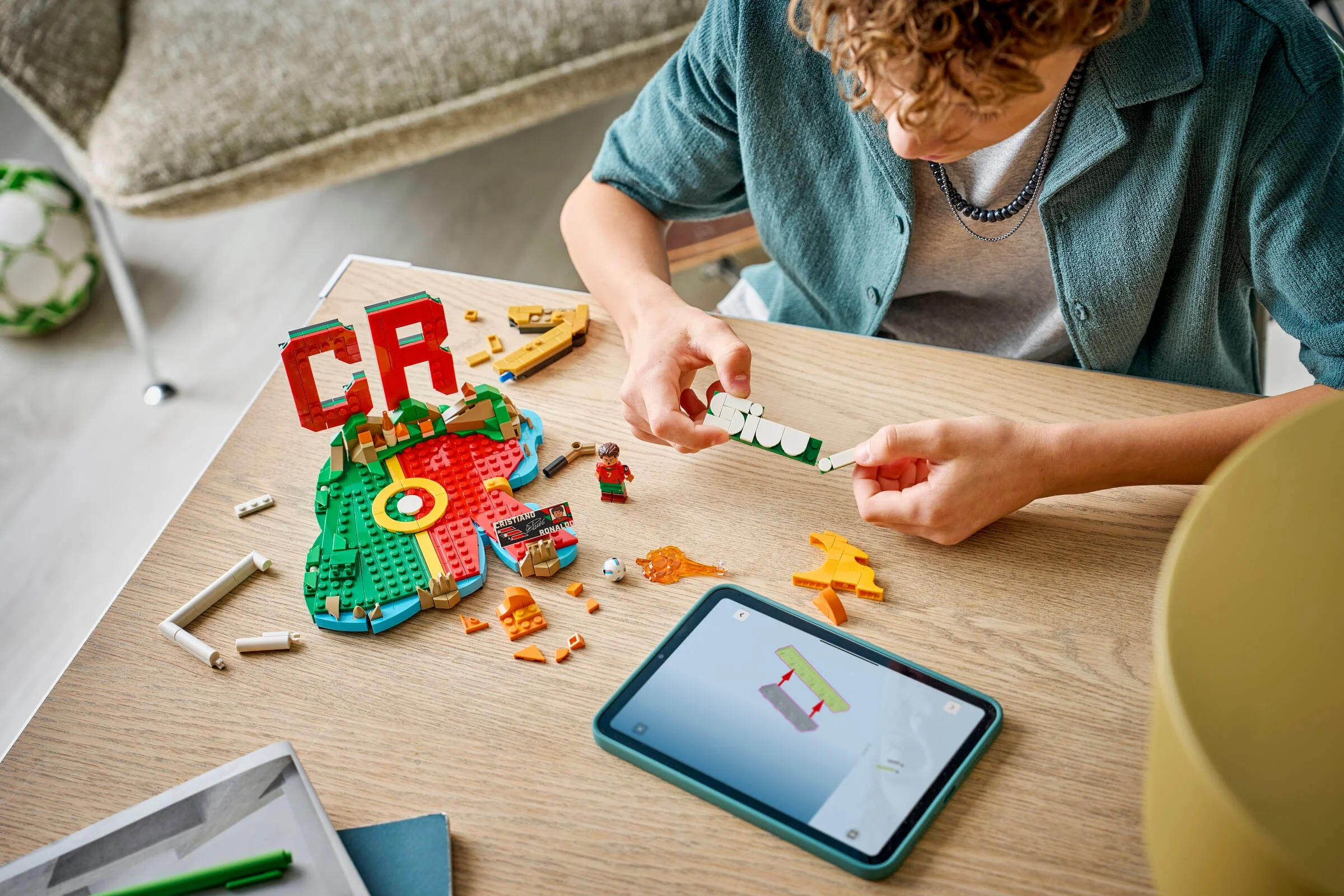 Imagine cu un tânăr construind setul LEGO Cristiano Ronaldo, folosind instrucțiuni pe tabletă.
