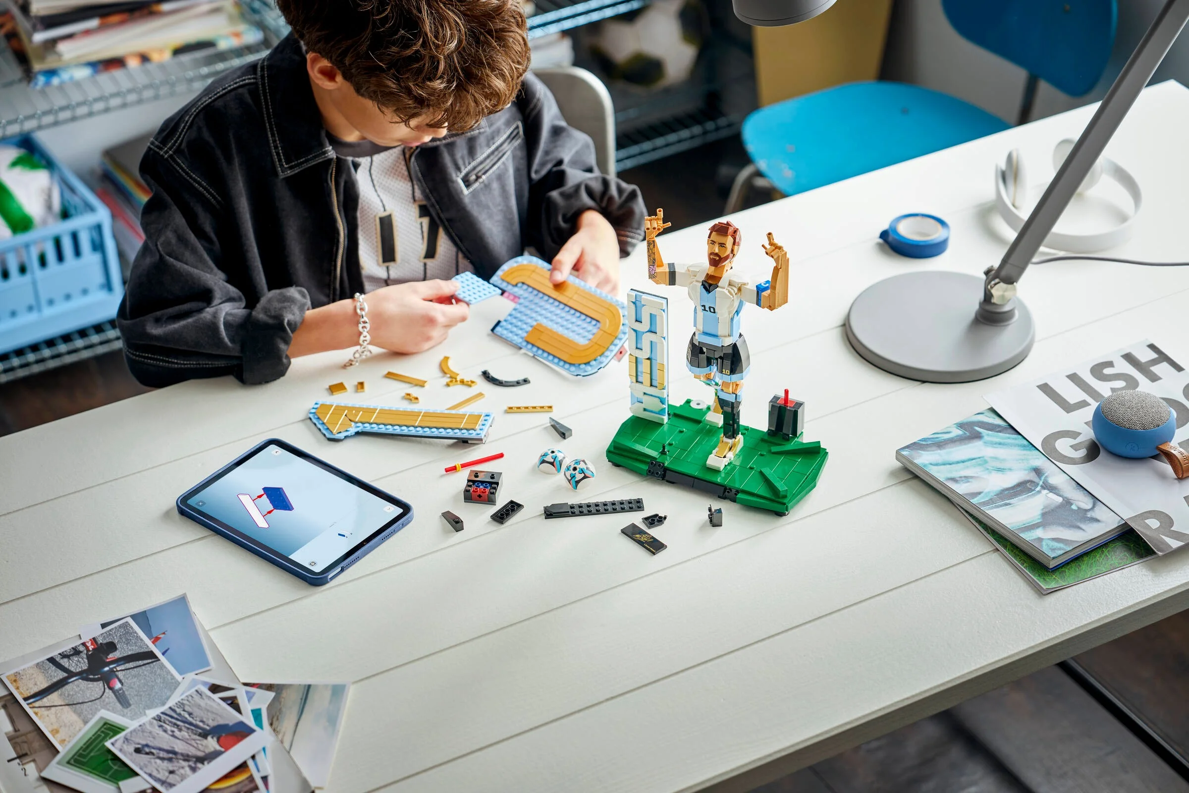 Copil construind setul LEGO Lionel Messi, cu instrucțiuni pe tabletă. Concentrare și creativitate.