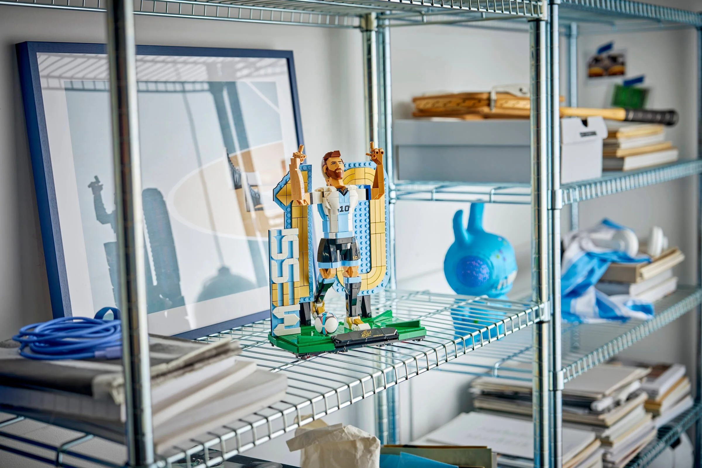 Modelul LEGO Lionel Messi pe un raft metalic, alături de alte obiecte. Un cadou inedit!