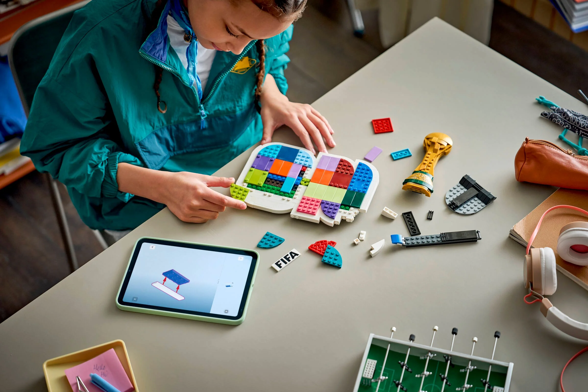 Fetiță construind emblema FIFA World Cup 2026 cu piese LEGO. Instrucțiuni pe tabletă.