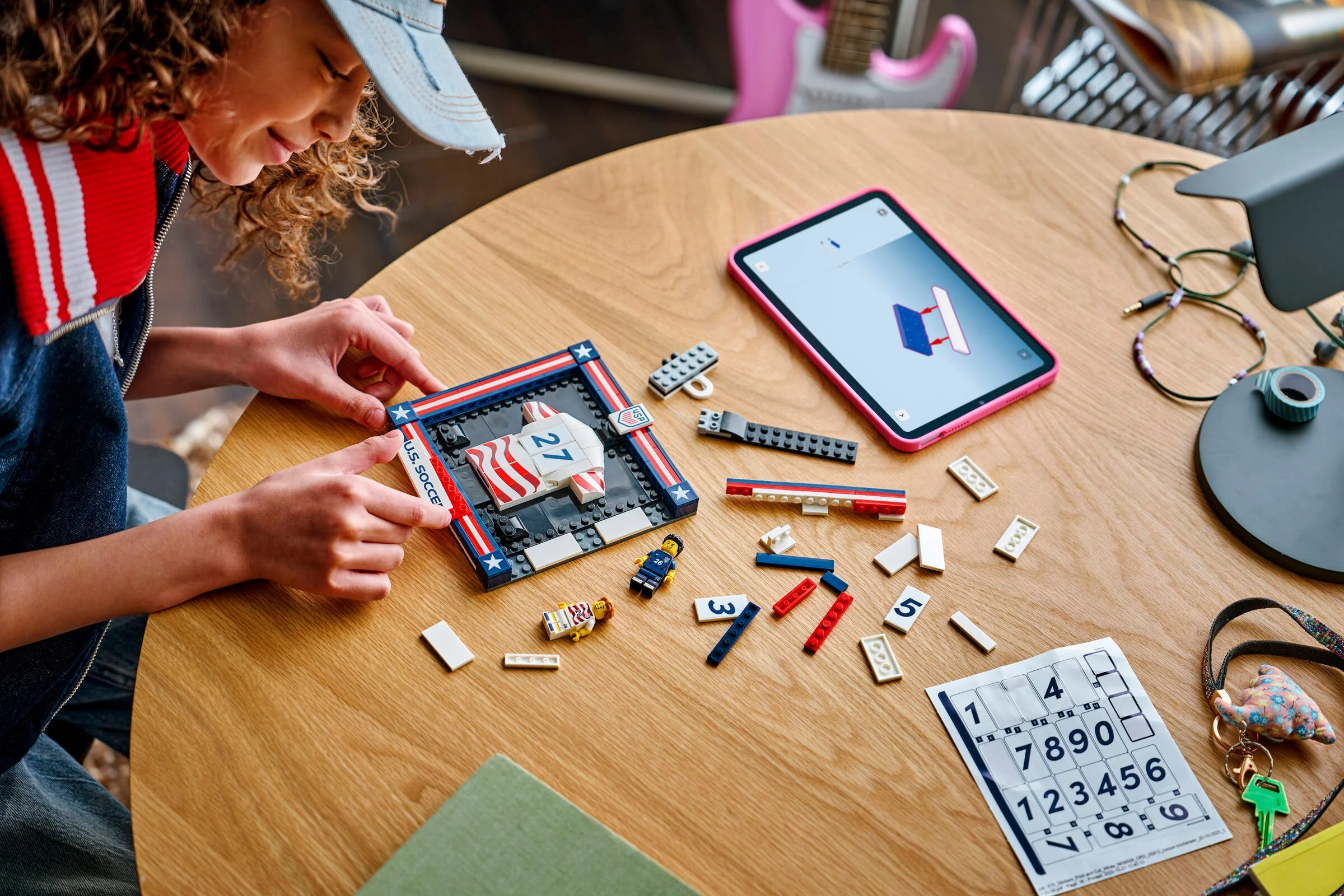 O fată construiește setul LEGO cu tricoul echipei SUA. Instrucțiuni digitale pe tabletă.