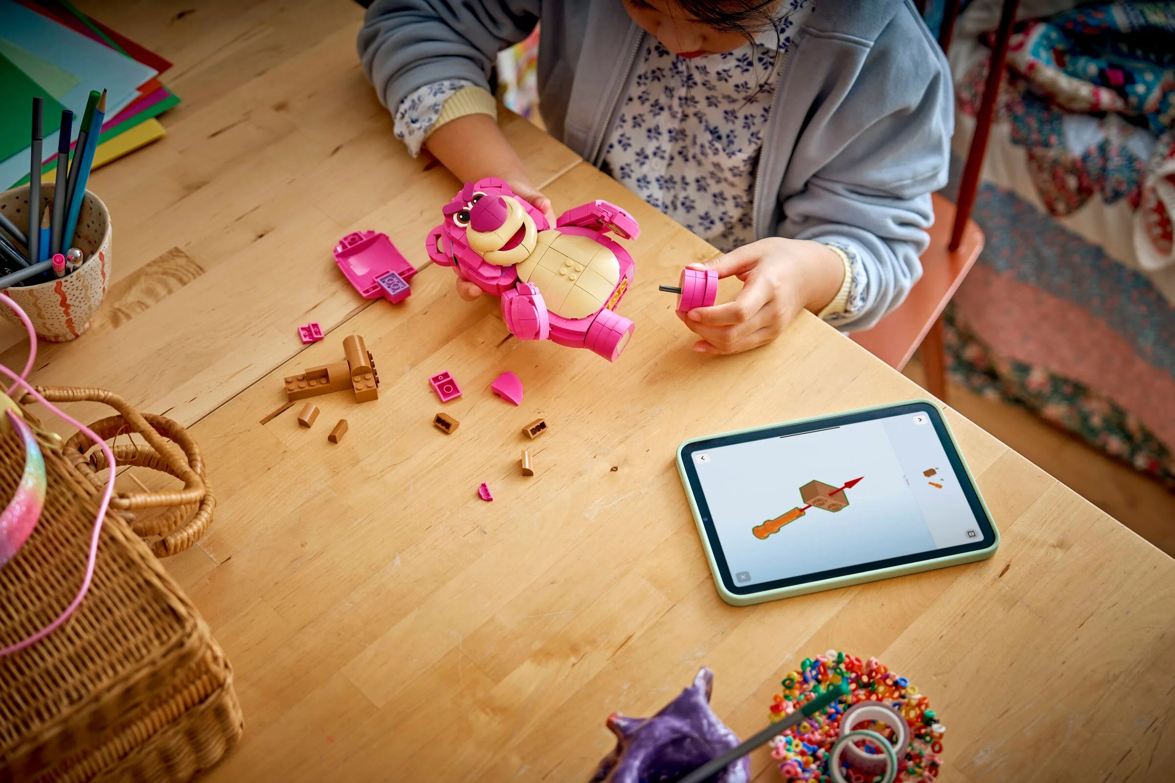 O fetiță construiește setul LEGO Lotso, folosind instrucțiuni de pe tabletă.