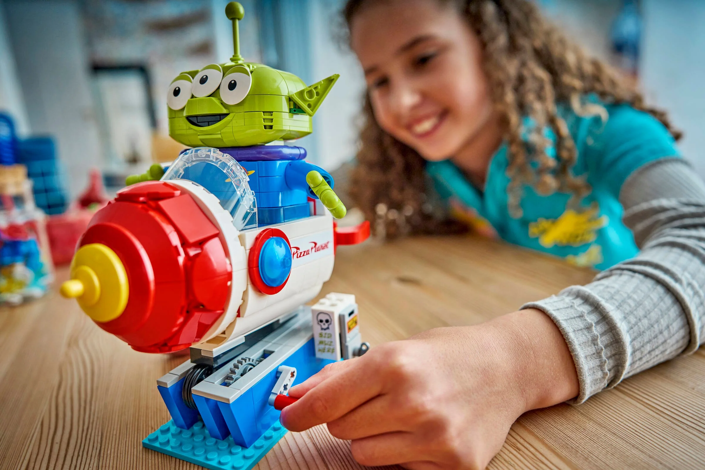 Imagine cu Alien și racheta Pizza Planet, set LEGO 43307, cu o fetiță zâmbind în fundal.