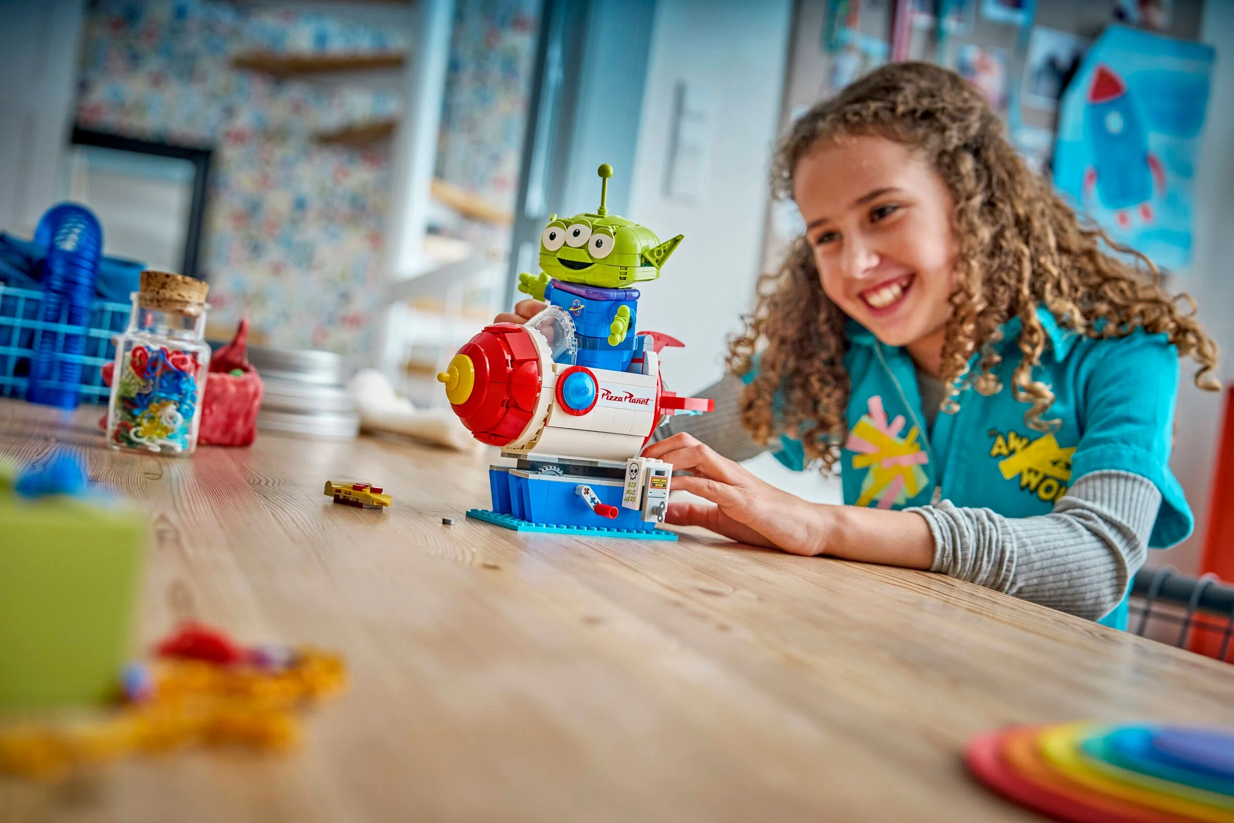 O fată zâmbitoare se joacă cu setul LEGO Alien cu rachetă Pizza Planet.