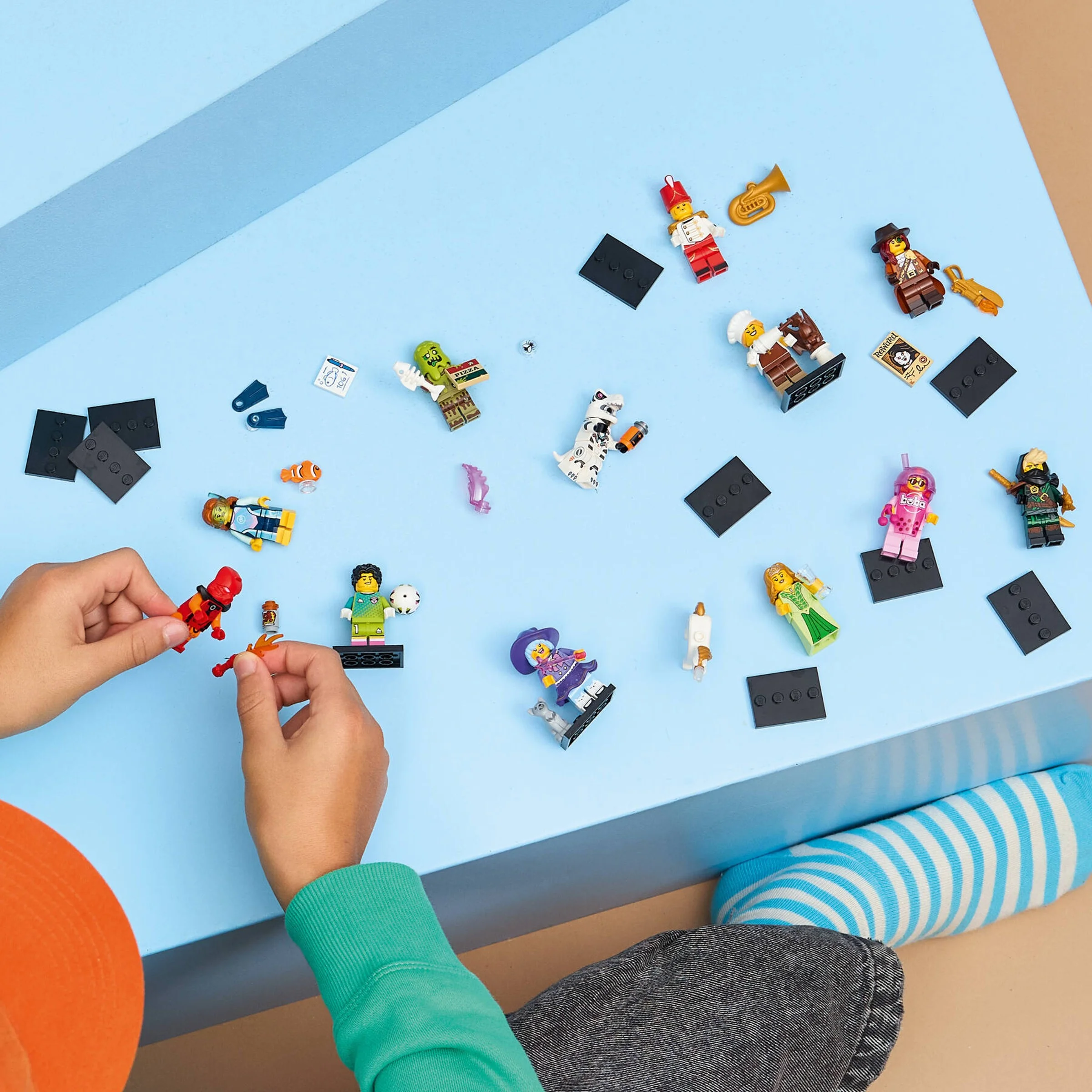 Imagine cu minifigurinele LEGO 71052, inclusiv Robot T. rex, așezate pe o suprafață albastră, cu o persoană care se joacă.