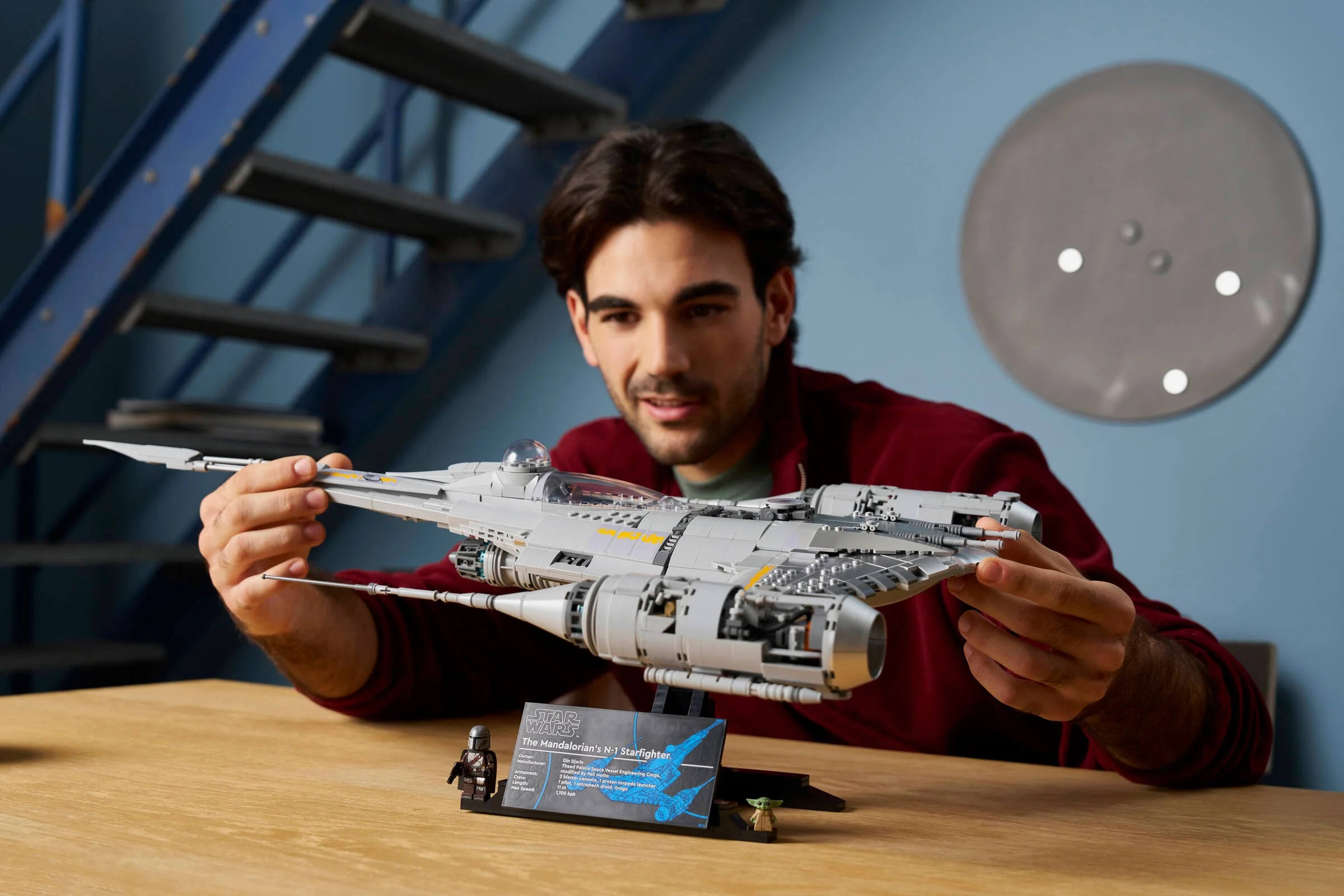 Bărbat prezintă N-1 Starfighter, setul LEGO 75442, alături de minifigurinele Mandalorian și Grogu.