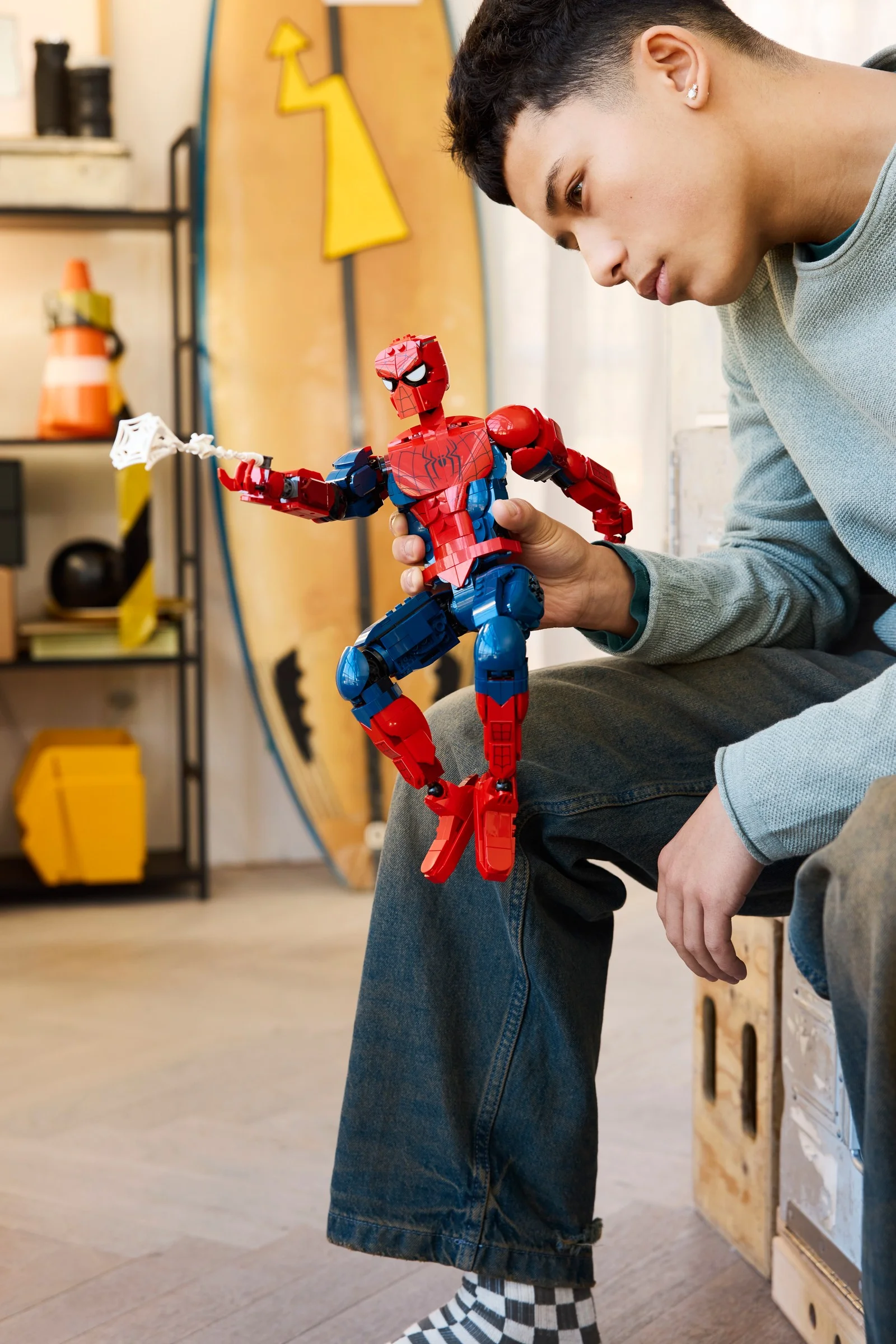 Băiat admirând figurina LEGO Spider-Man, roșie și albastră, cu pânză.