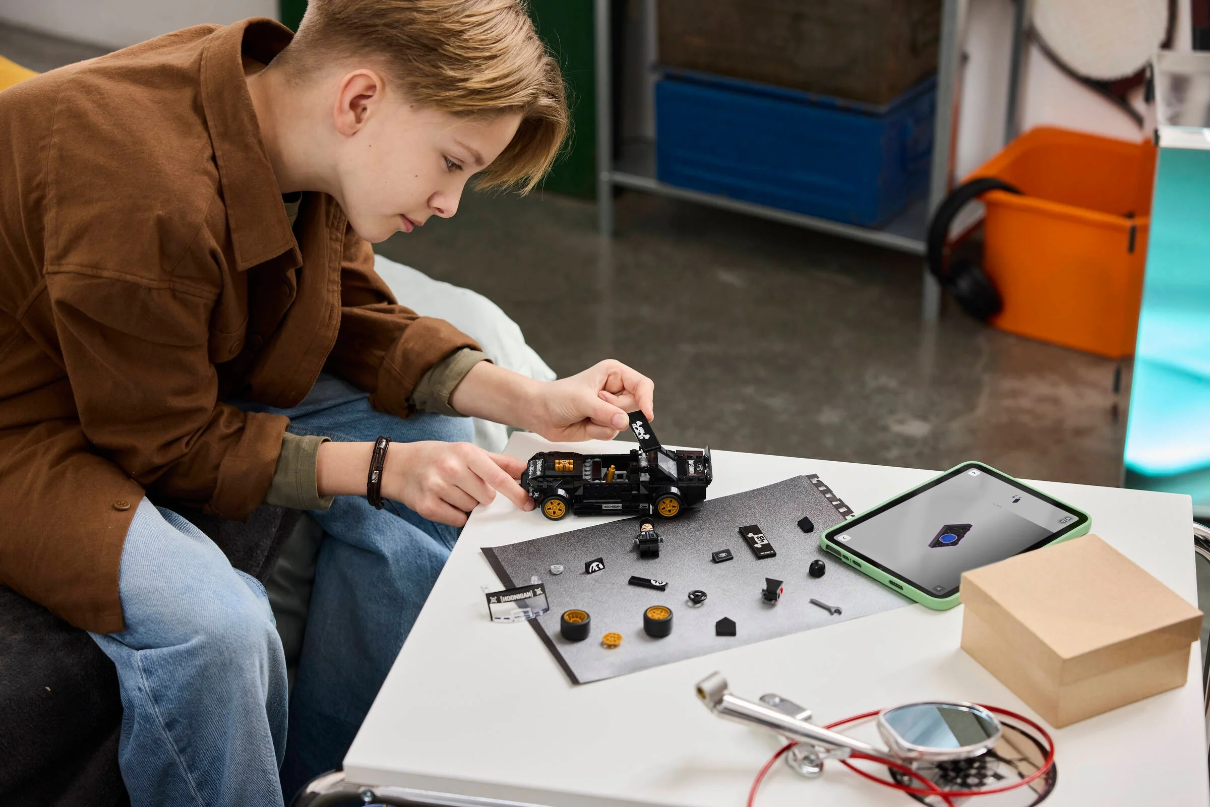 Un copil asamblează modelul LEGO Hoonicorn, urmând instrucțiunile de pe o tabletă digitală.
