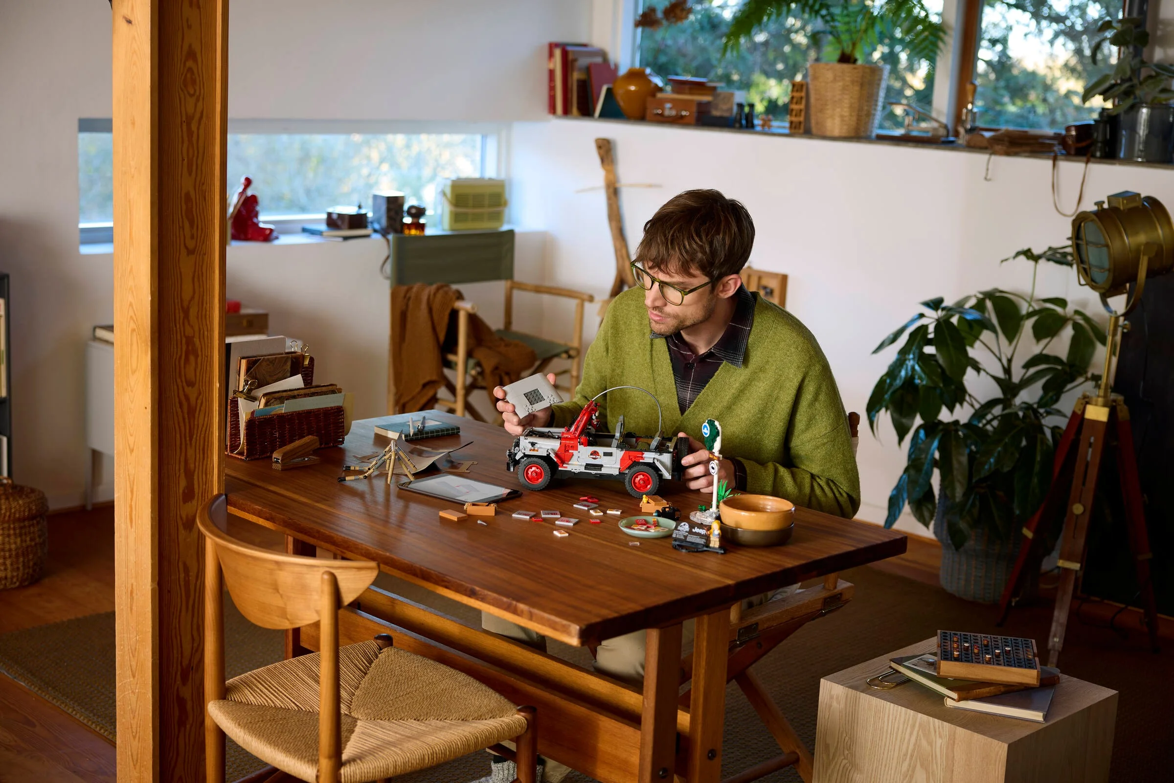 Bărbat construind Jeep-ul Jurassic Park LEGO 77984 pe o masă din lemn. Detaliile includ minifigurine și accesorii.