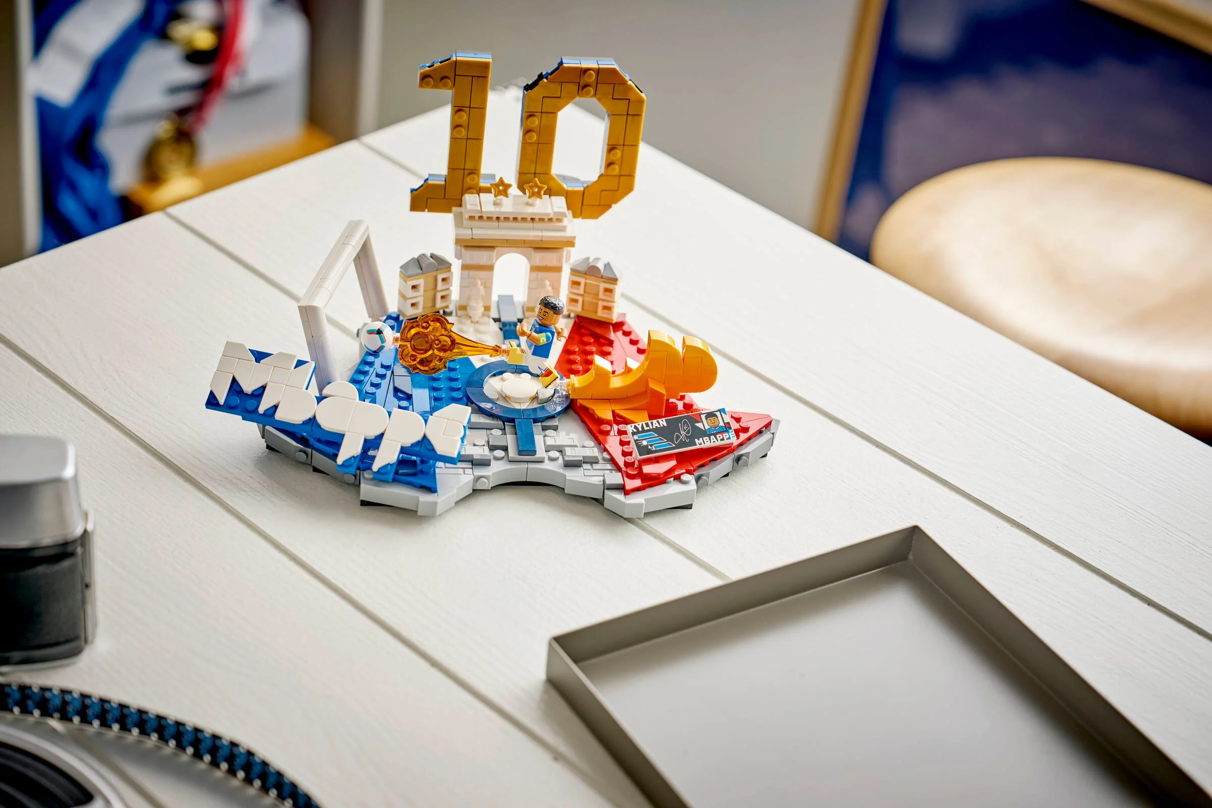 O vedere detaliată a modelului LEGO Kylian Mbappé pe o masă. Elemente distinctive: Arcul de Triumf, numărul 10.