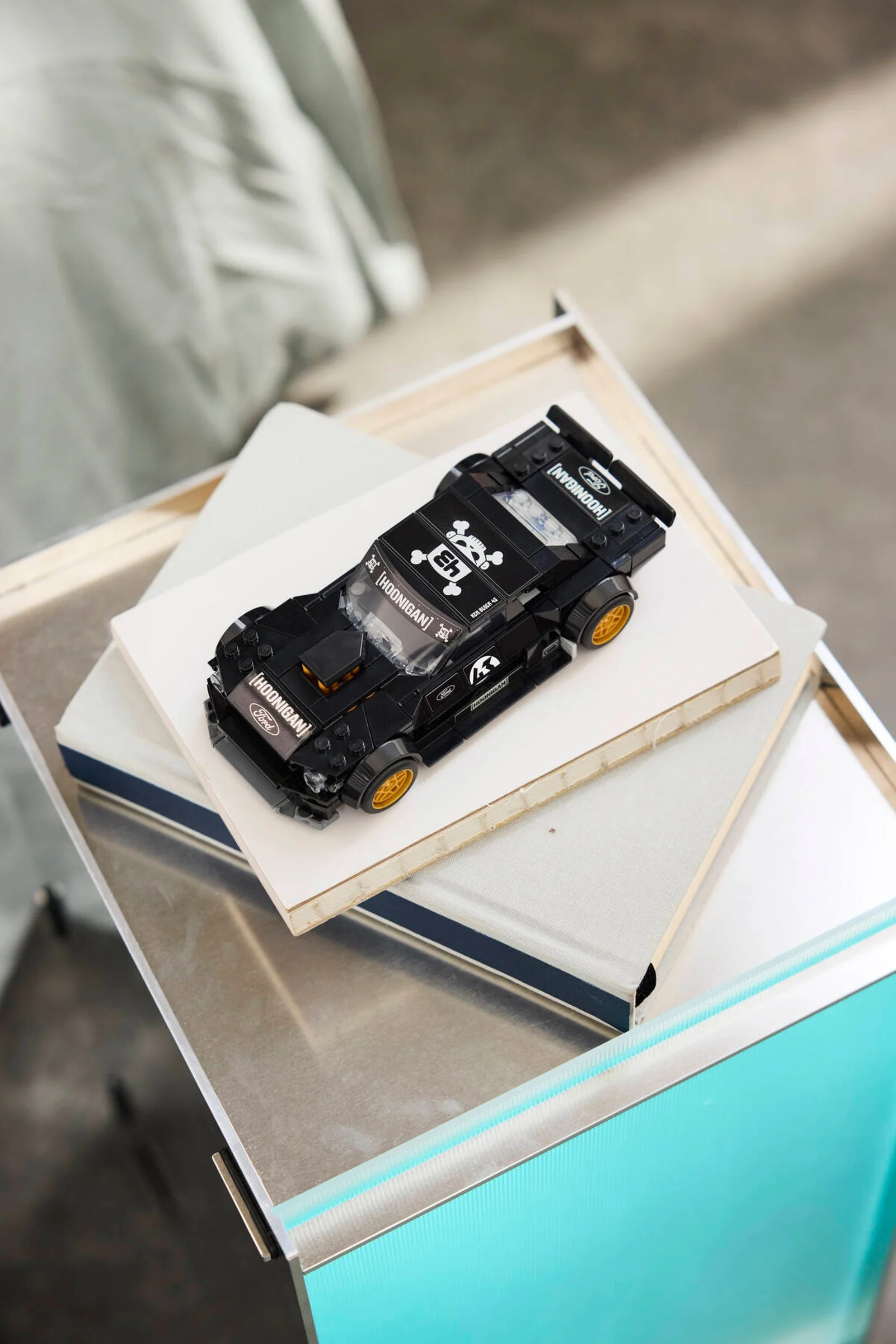 Mașina LEGO Ford Mustang Hoonicorn RTR V1, neagră, cu detalii și logo-uri, așezată pe cărți albe.