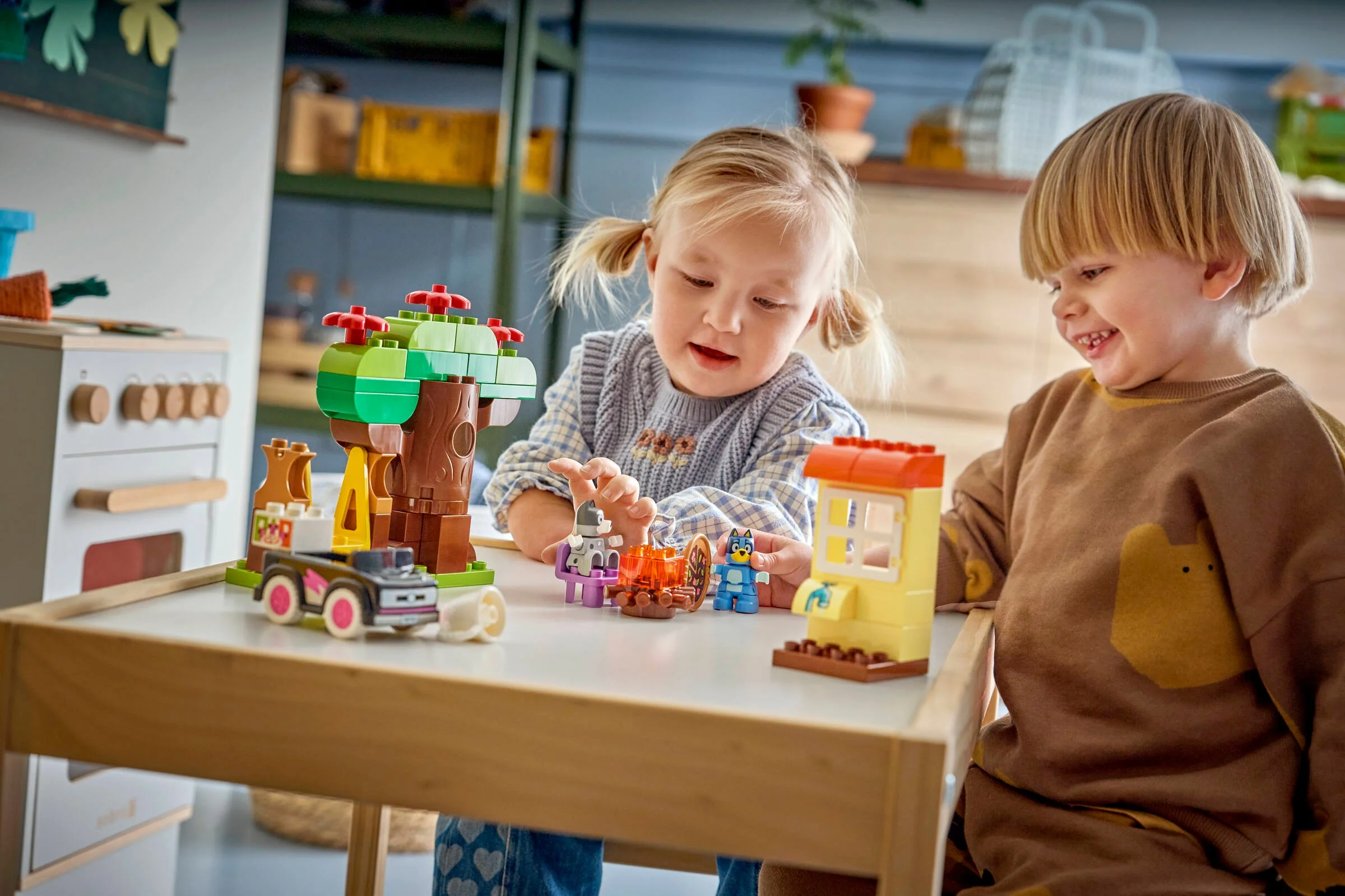 Doi copii se joacă cu setul LEGO DUPLO 10469, Pizza Girls cu Muffin și Bluey, zâmbitori și entuziasmați.