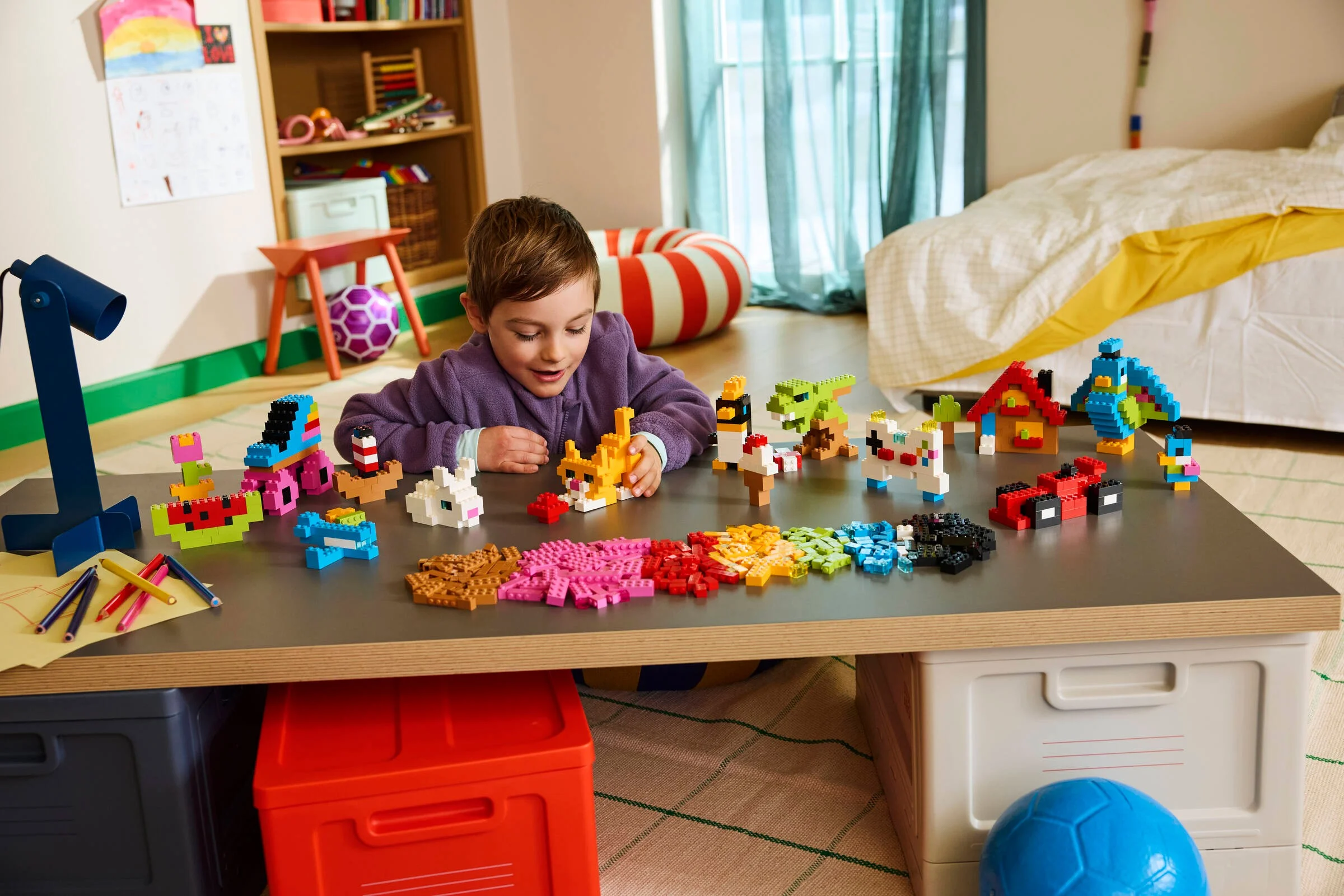 Un băiat construiește cu cărămizi LEGO colorate pe o masă. Modele mici sunt aranjate. Distracție creativă.