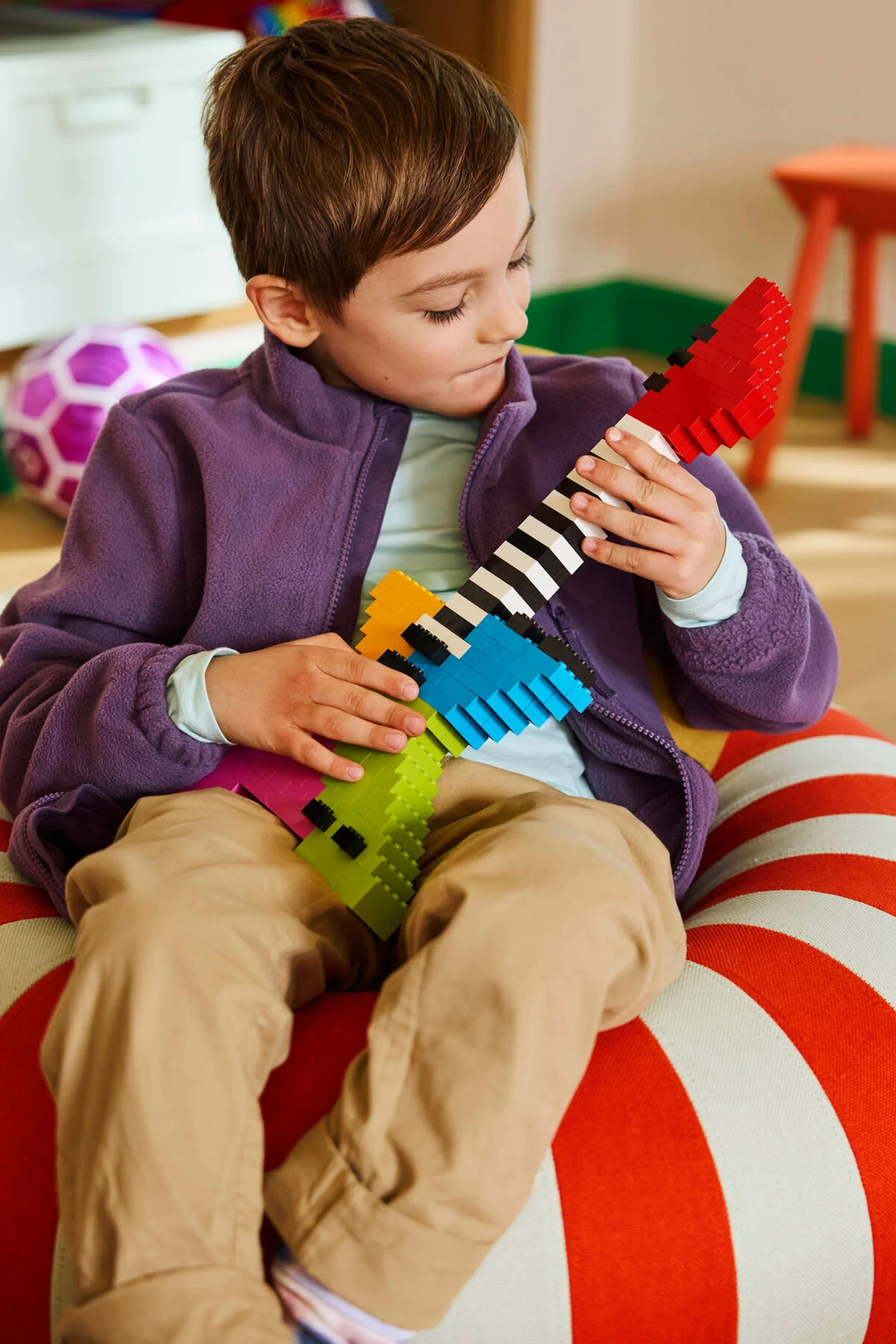 Băiat se joacă cu o chitară construită din cărămizi LEGO colorate. Distracție creativă.