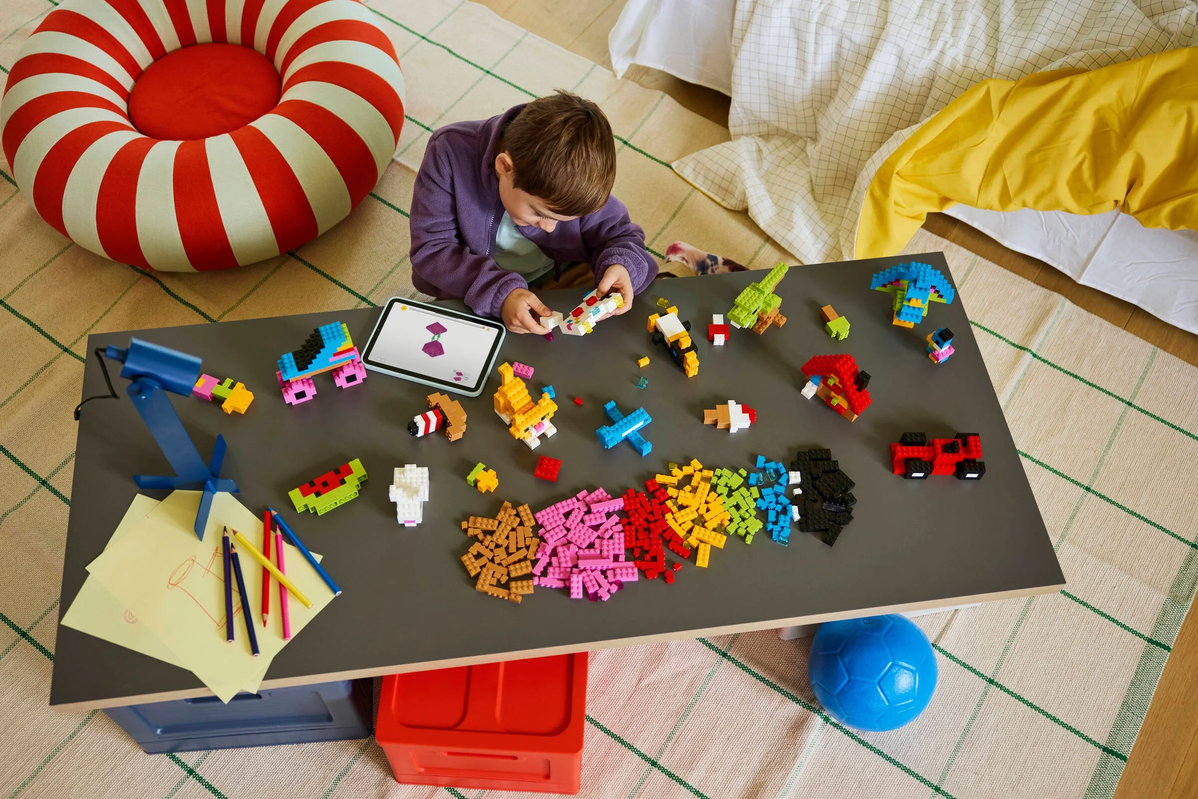 Copil construind cu cărămizi LEGO colorate pe o masă. Setul 11045 este perfect pentru creativitate.