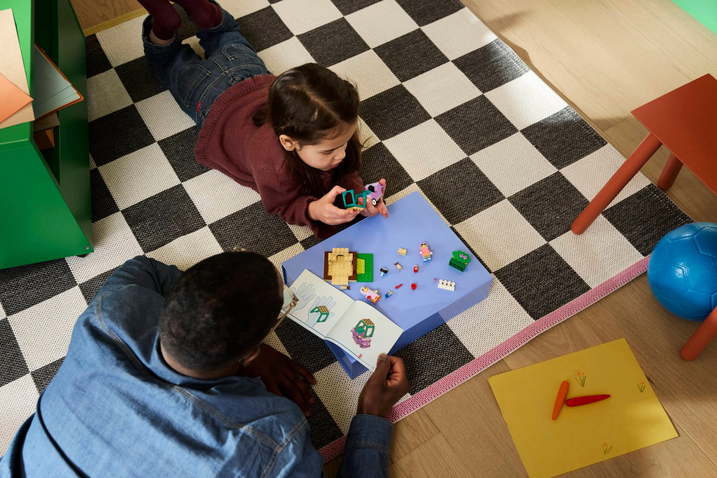 O fetiță și un adult construiesc setul LEGO Bluey cu piese așezate pe o măsuță albastră.