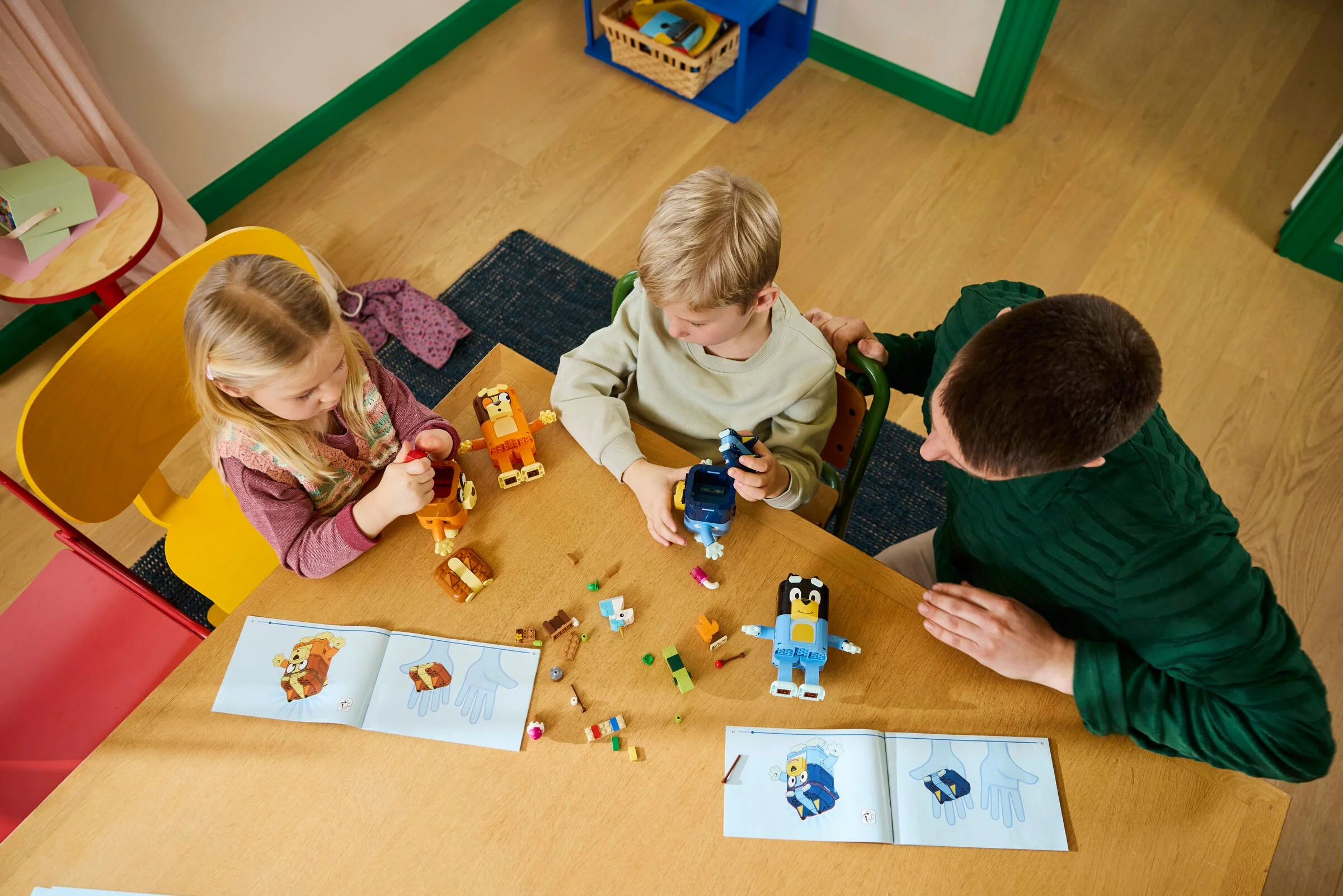 Copii și un adult construind setul LEGO Bluey. Imagine din unghi înalt, familie la masă.