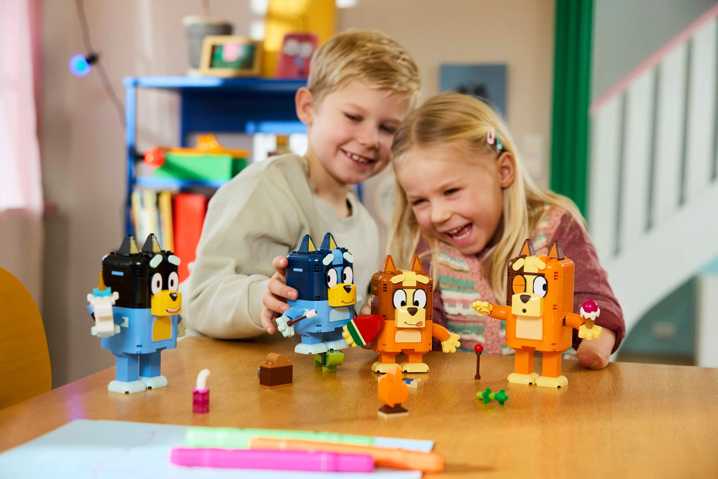 Copii zâmbitori se joacă cu figurinele LEGO Bluey construite din cărămizi.