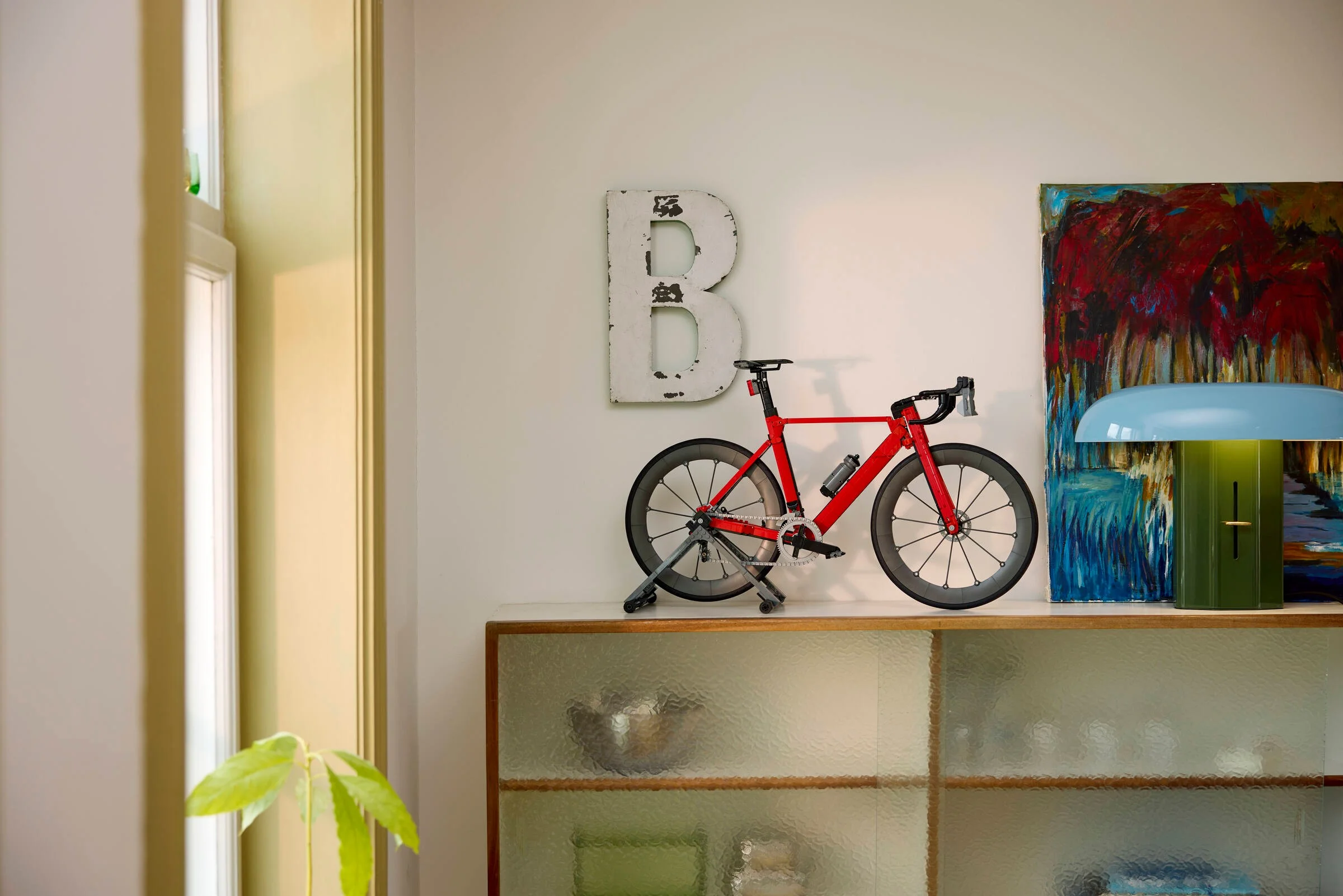 O bicicletă de curse roșie LEGO pe un raft într-o cameră cu decor modern. Design atrăgător și detaliat.