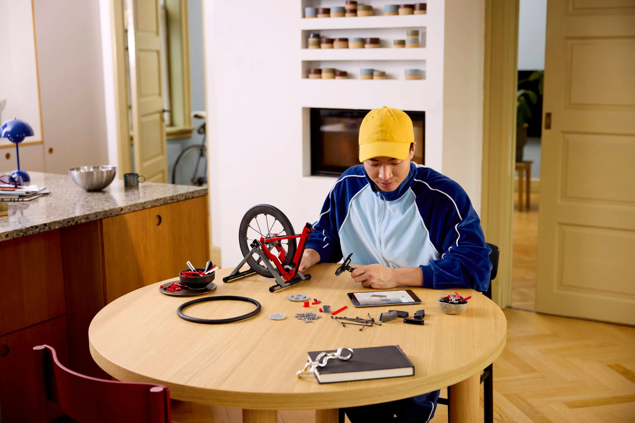 Persoană construind bicicleta LEGO, văzută de sus, piesele fiind împrăștiate pe masă.