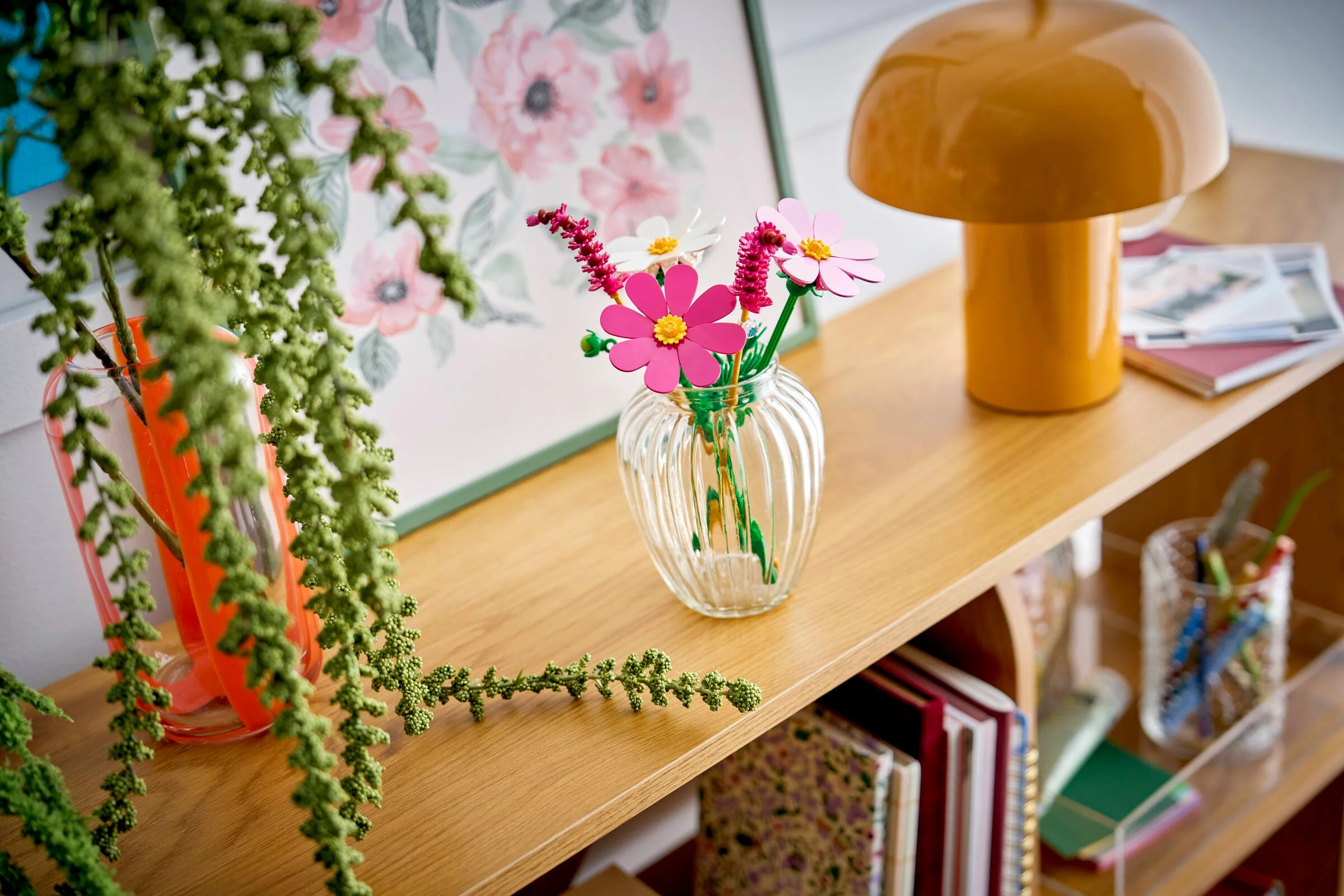 Cosmos Flowers LEGO aranjați într-o vază transparentă, așezați pe o etajeră.