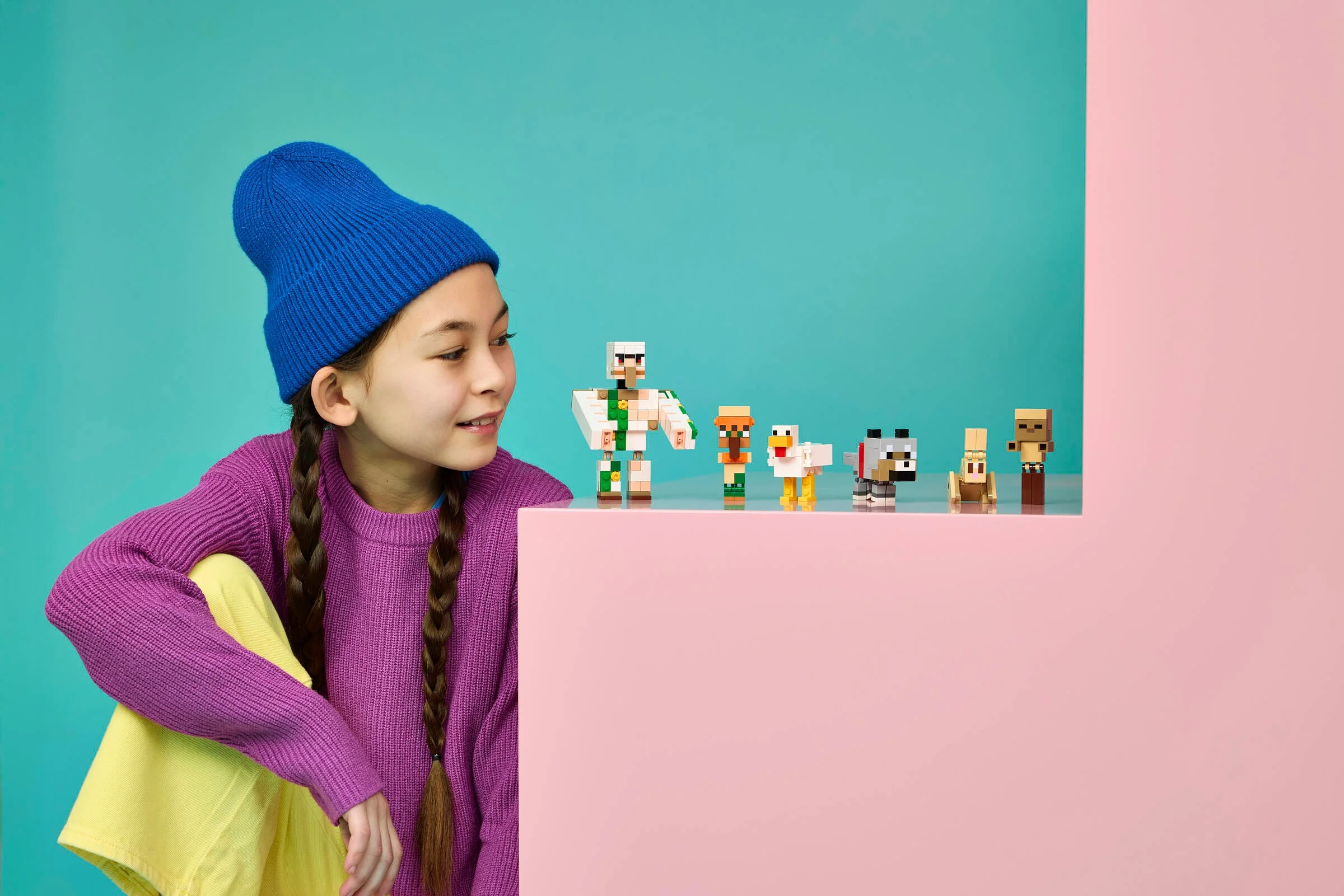 O fată se uită la figurinele LEGO Minecraft: Iron Golem, Chicken Jockey, pui, lup și un zombie bebeluș.