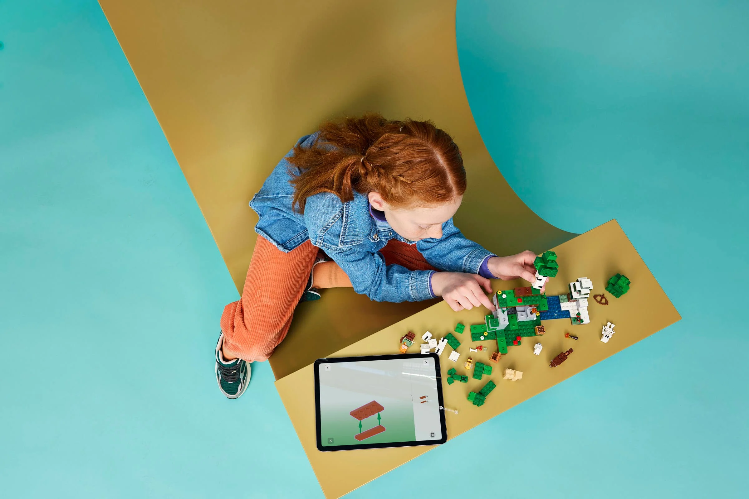 Fată construind setul LEGO Minecraft 21593. Se vede modelul și instrucțiunile digitale pe tabletă.