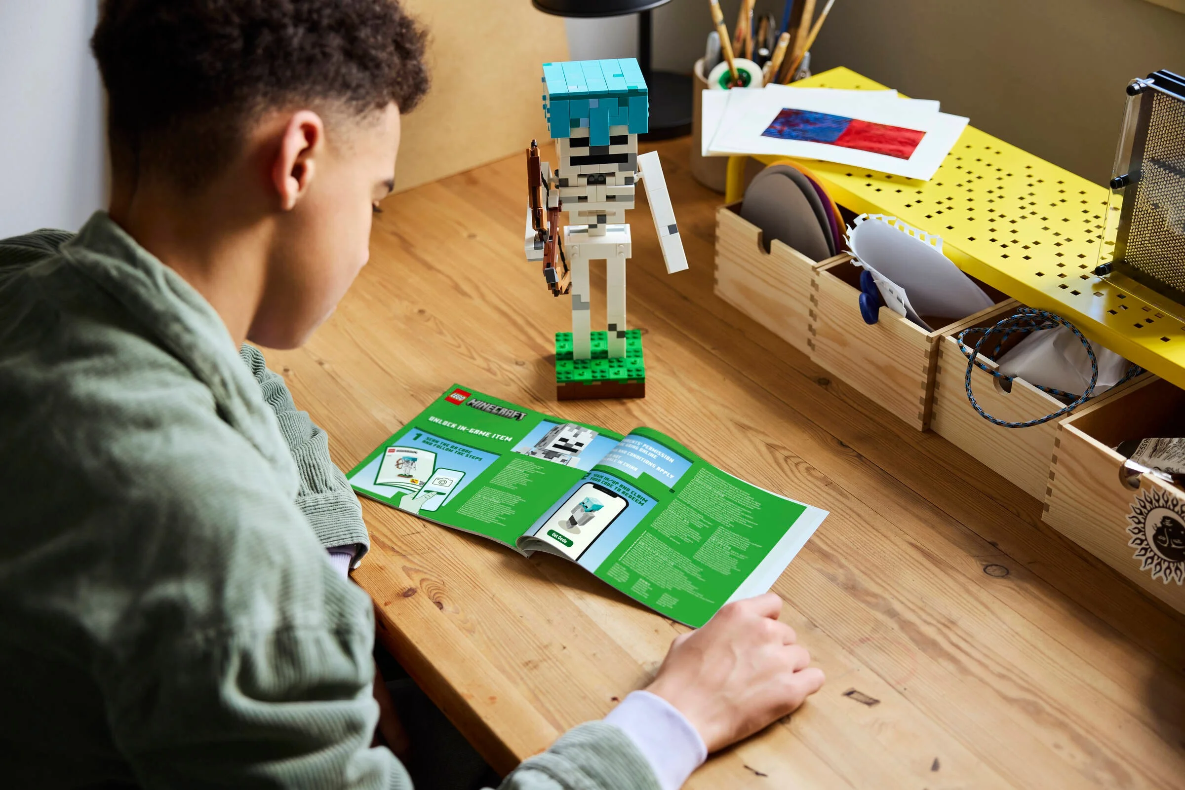 Un băiat se uită la instrucțiunile LEGO Minecraft Skeleton, lângă modelul construit.