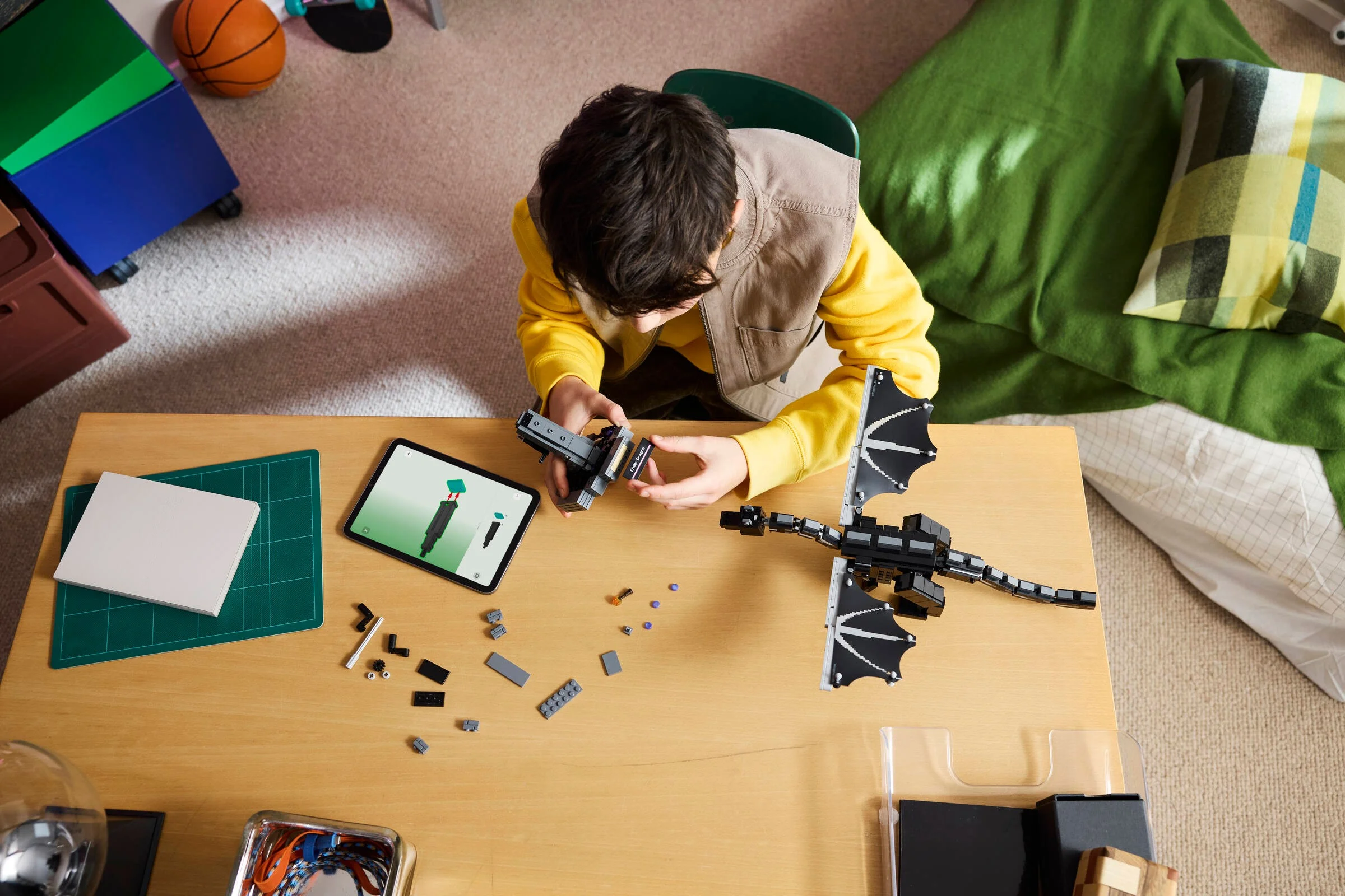 Copil construind Ender Dragon LEGO. Imagine de sus, concentrat pe construcție.