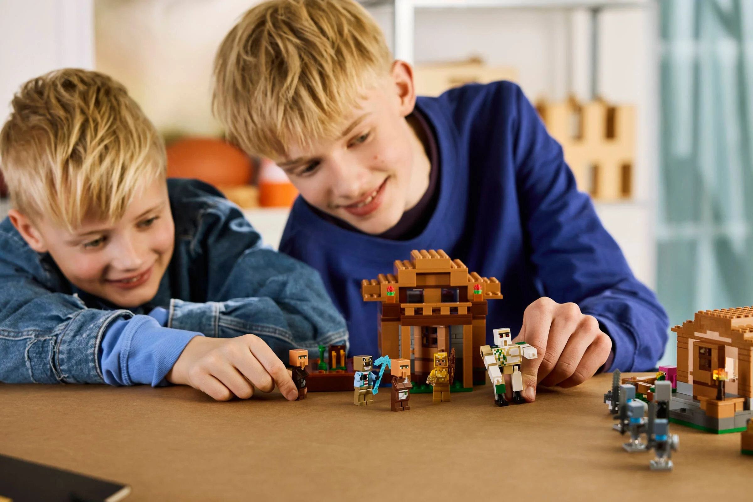 Doi copii se joacă cu setul LEGO Minecraft Atacul asupra satului.