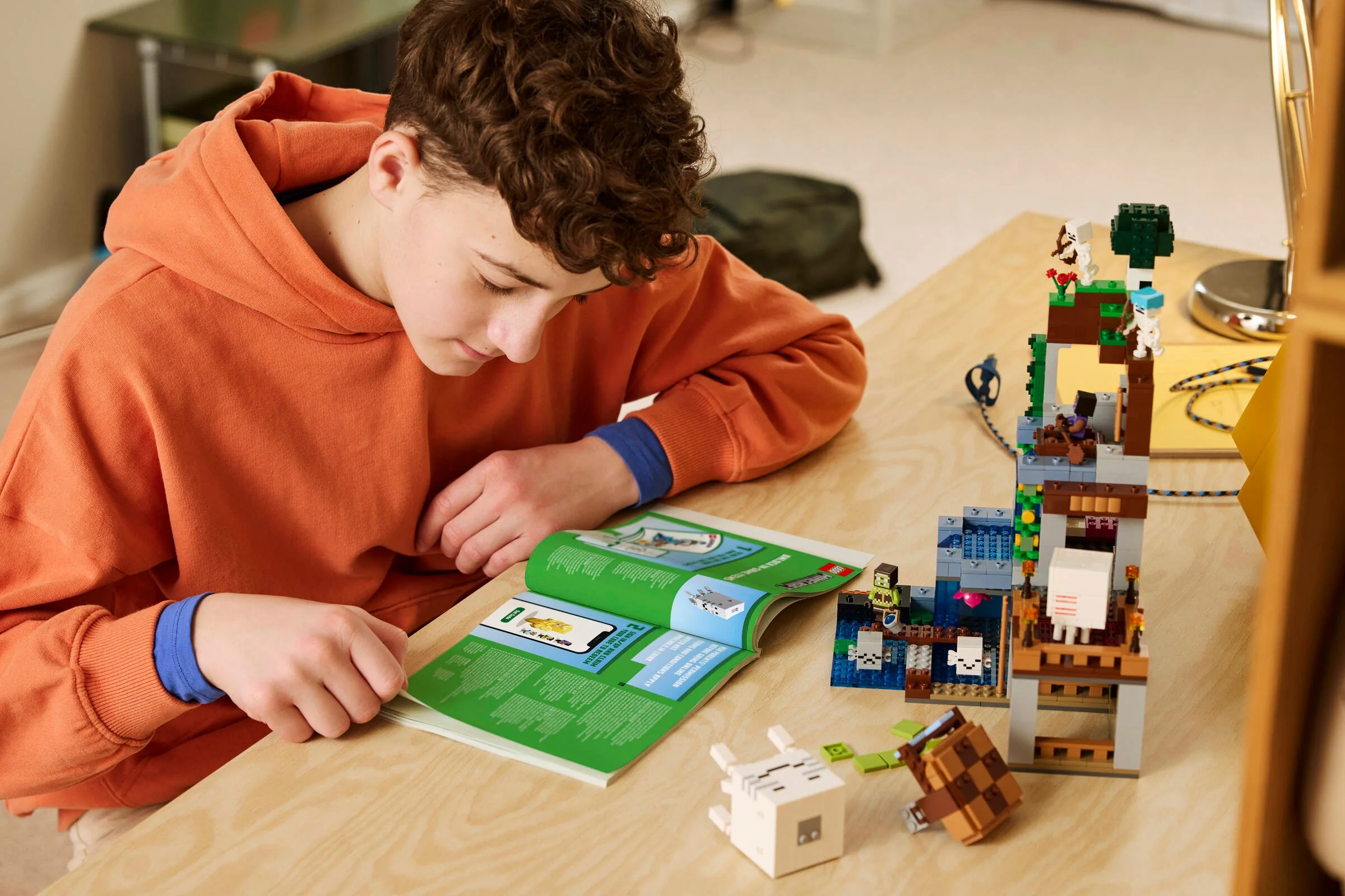 Copil construind setul LEGO Minecraft 21597 „Stația Ghast”, urmând instrucțiunile din manual.