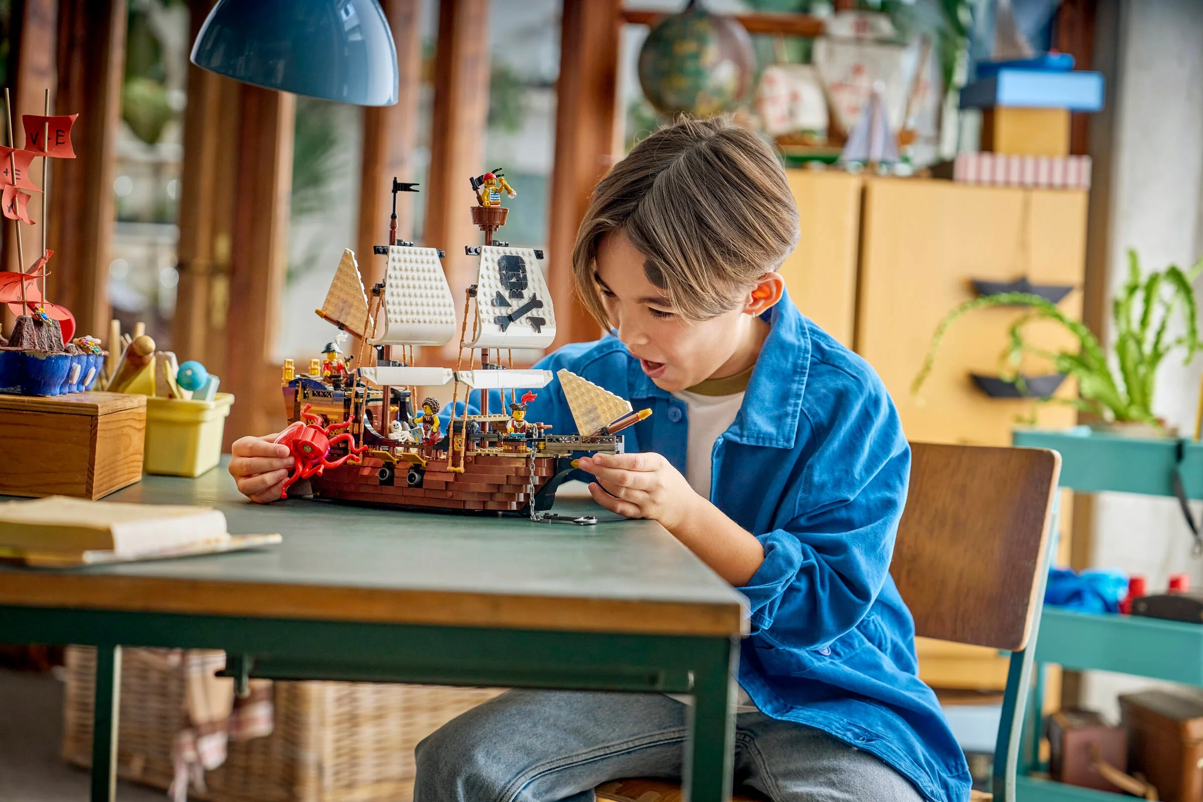 Băiat construind corabia de pirați LEGO 31387. Model detaliat, plin de aventură.