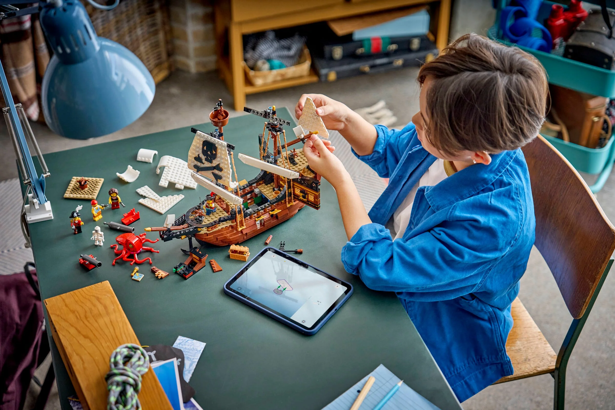Copil construind corabia de pirați LEGO. Construcție detaliată și minifigurine vizibile.