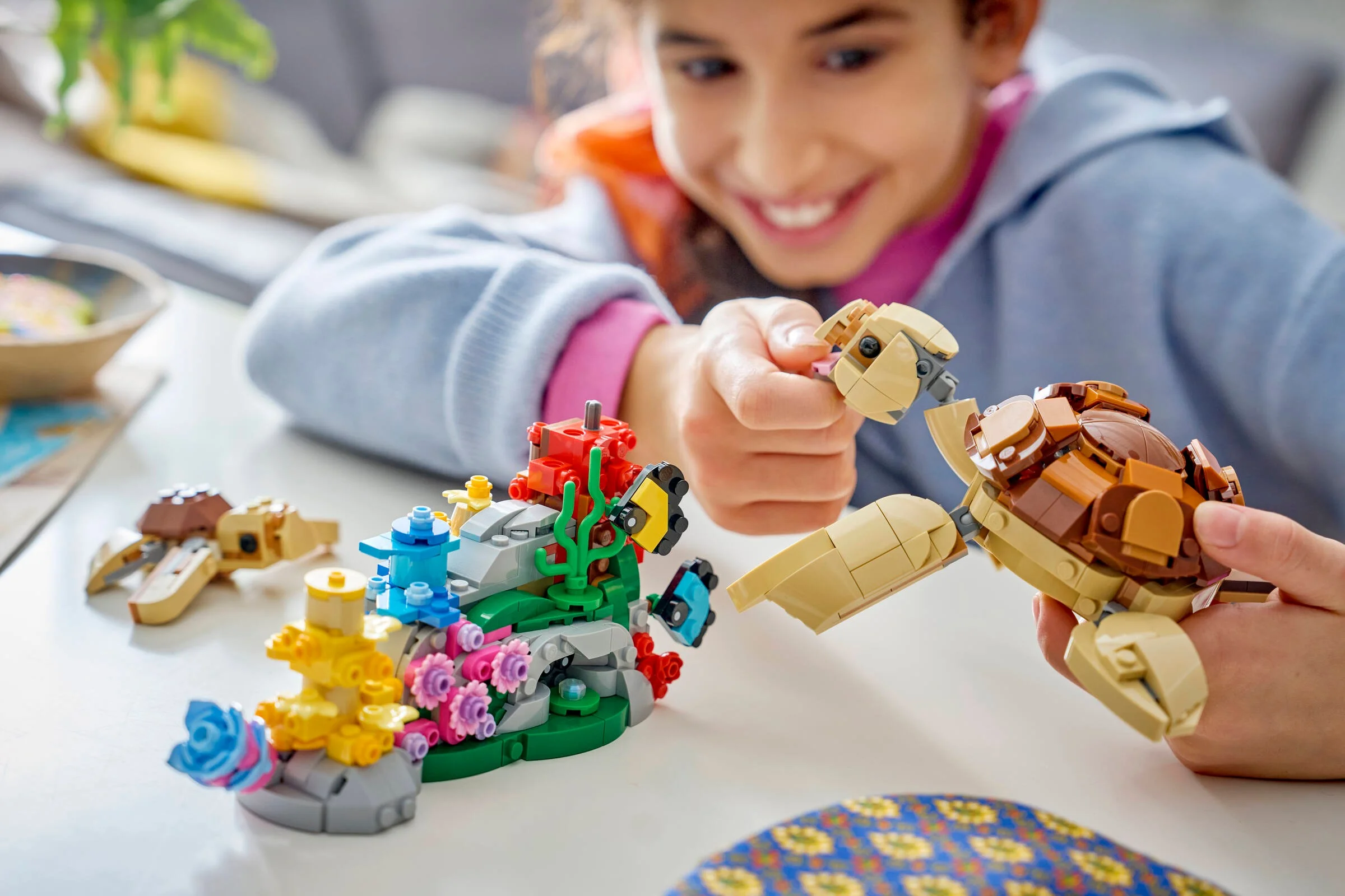 Copil zâmbitor interacționând cu setul LEGO: țestoase și recif de corali detaliat.