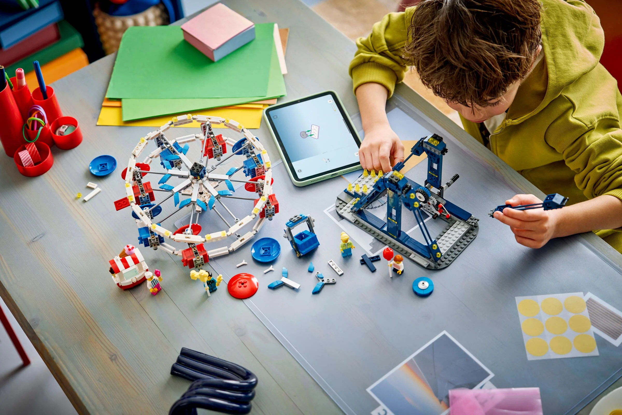 Copil asamblând setul LEGO Ferris Wheel, urmând instrucțiunile de pe tabletă.